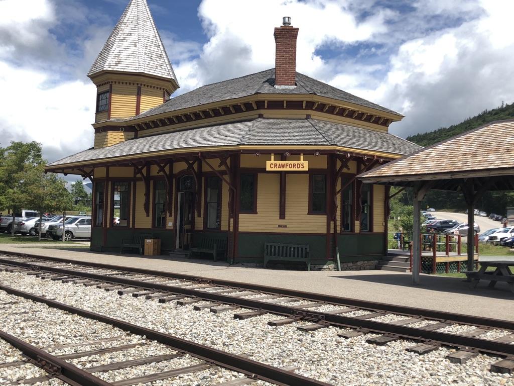 A historic yellow and green train station with tracks under a bright sky.