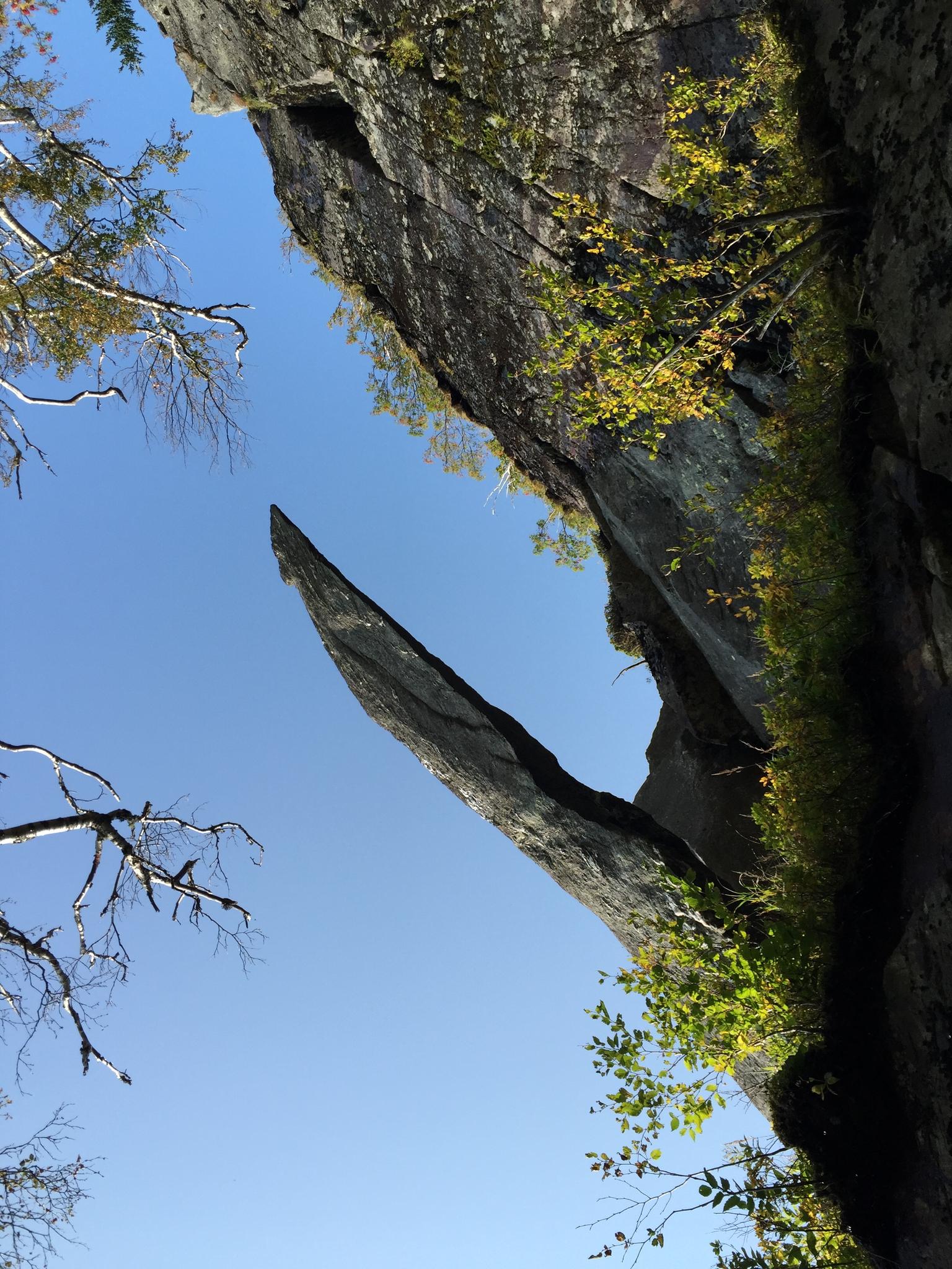 A sharp rock spire juts from a cliff against a clear blue sky.