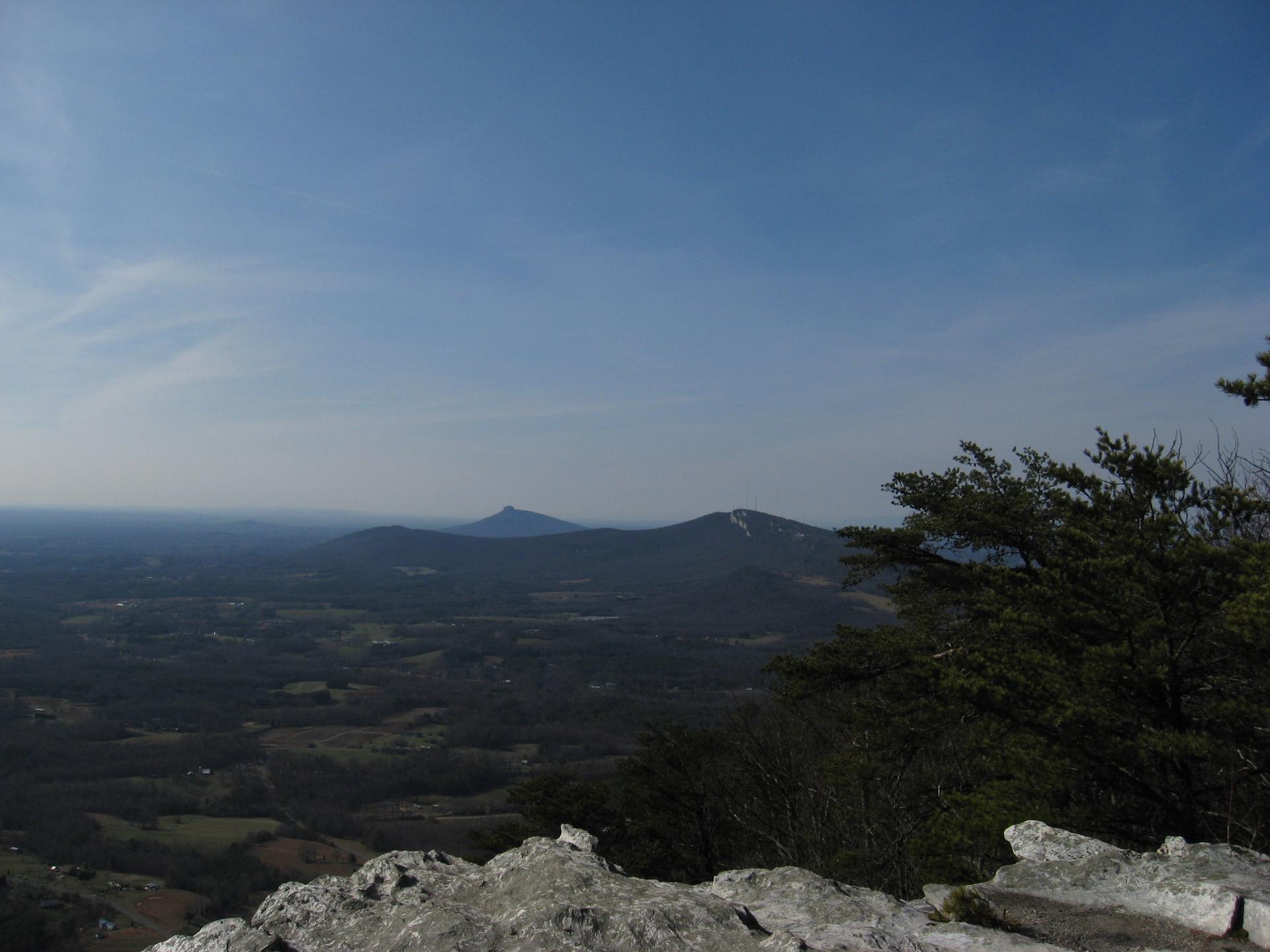 Distant hazy mountains and valley from rocky outcrop under clear blue sky.
