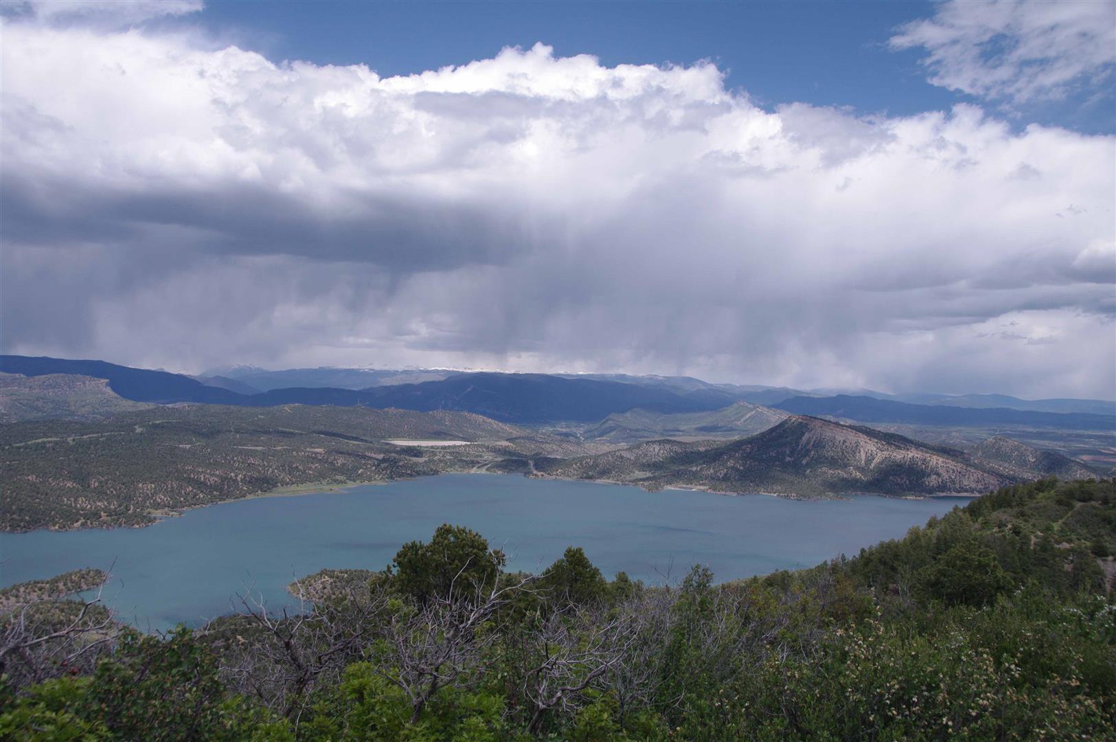 Panoramic view of a lake and mountains under a dramatic, stormy sky.