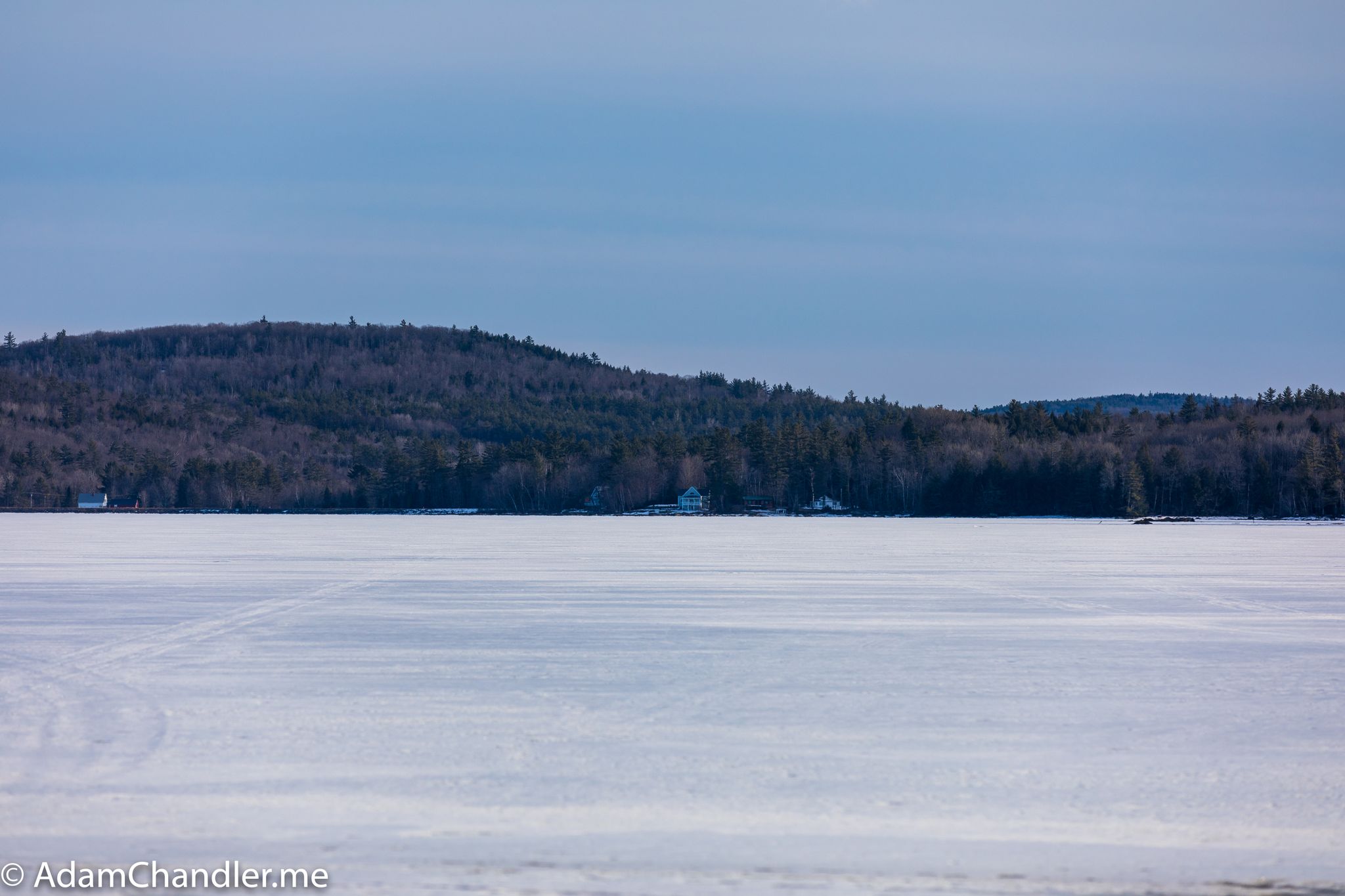 Expansive frozen lake with snow, backed by forested hills under a clear blue sky. - Goose Pond – Goose Pond loop from Goose Pond Dam