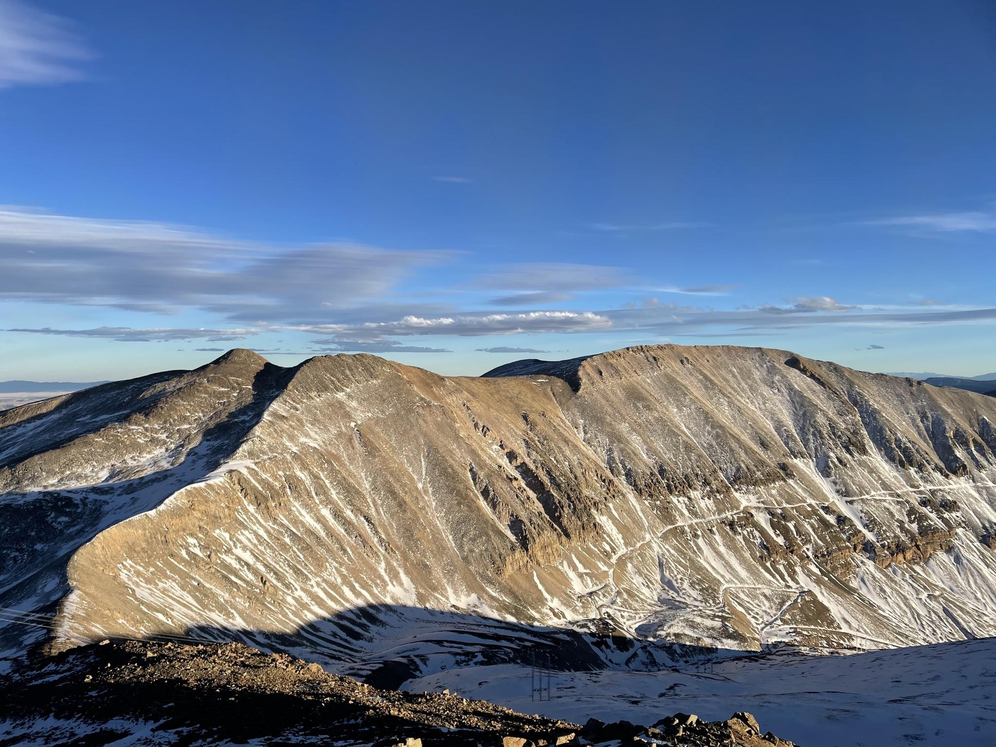 Snow-dusted mountain range with long shadows under a bright blue sky.