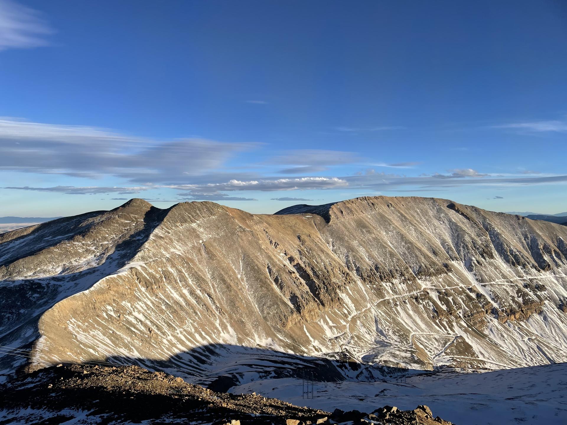 Snow-dusted mountain range with long shadows under a bright blue sky.