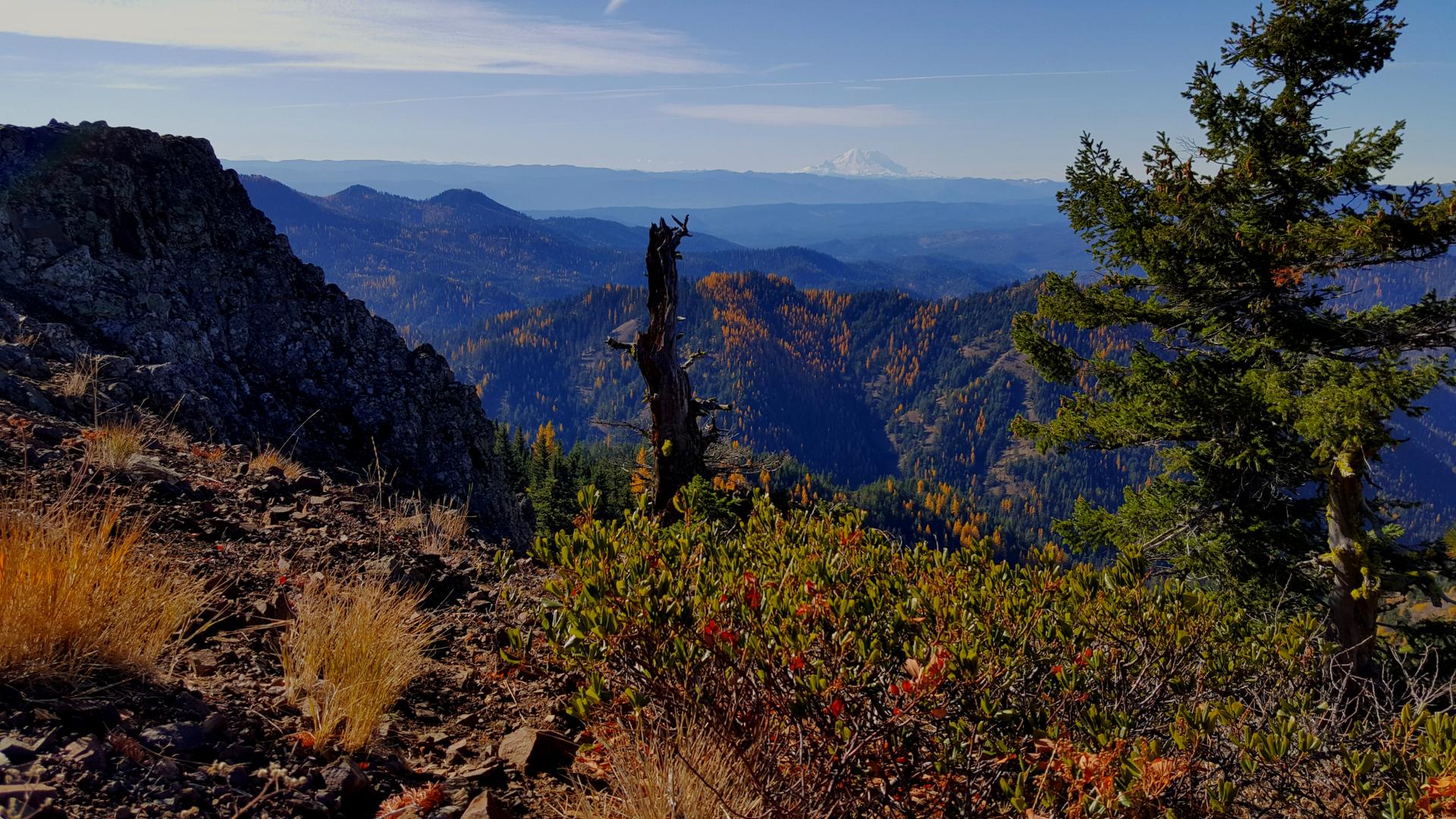 A vast mountain landscape with rocky foreground and distant peaks under a bright sky.