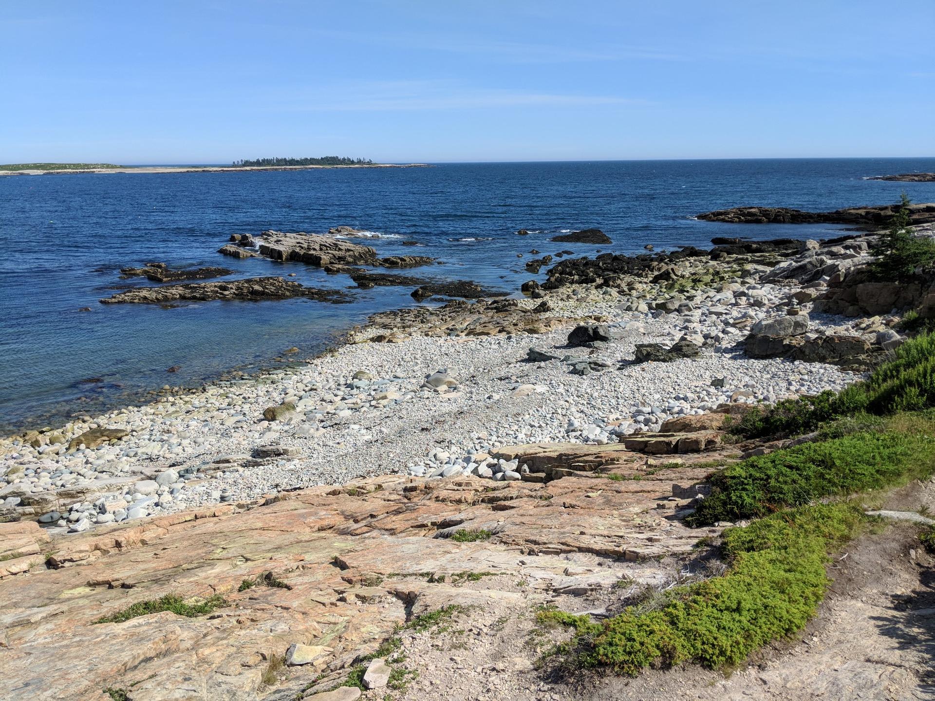 Sunny view of a rocky and pebbly beach meeting clear blue ocean water.