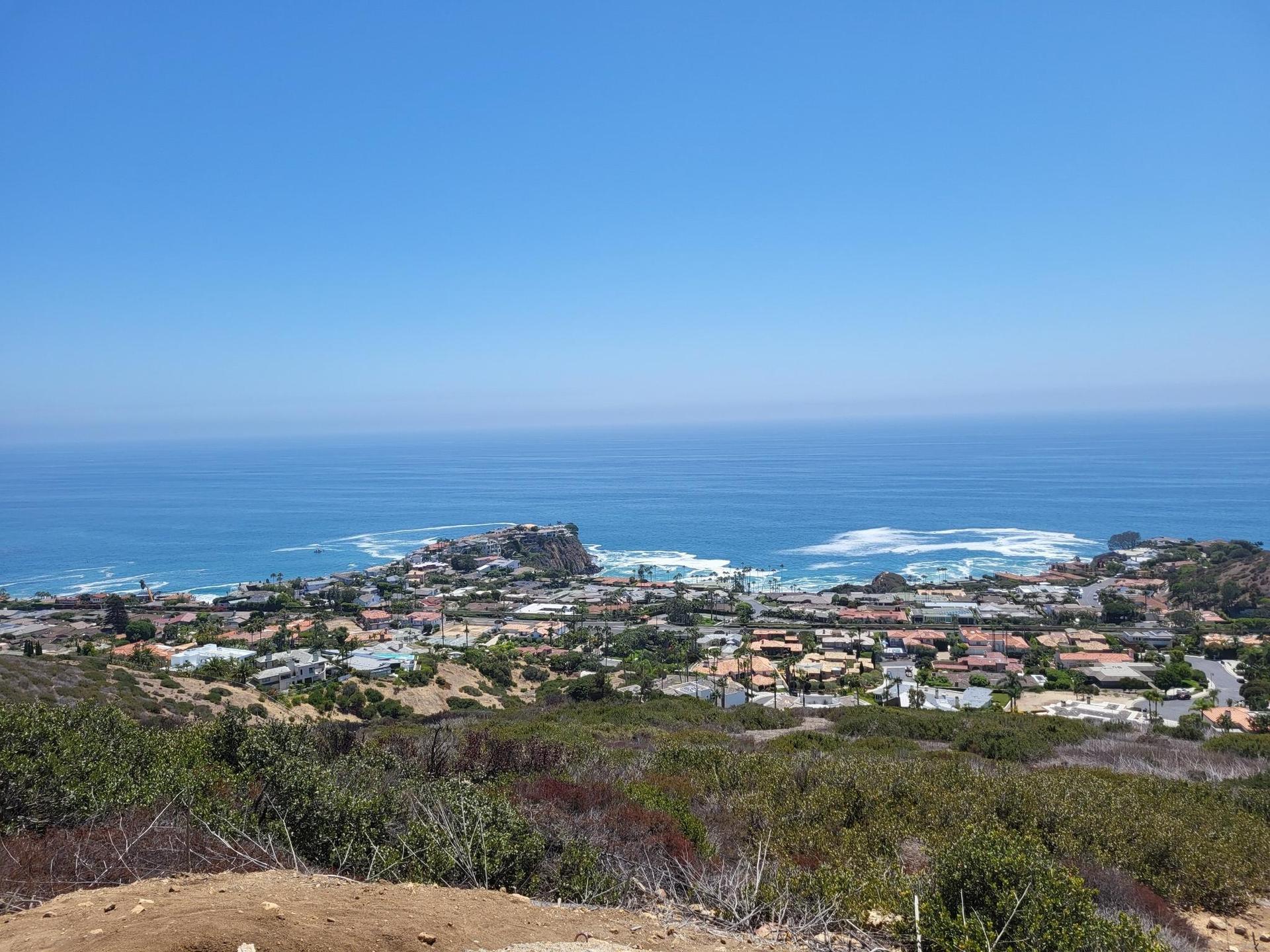 Coastal town nestled by a blue ocean with waves, seen from a dry hillside.