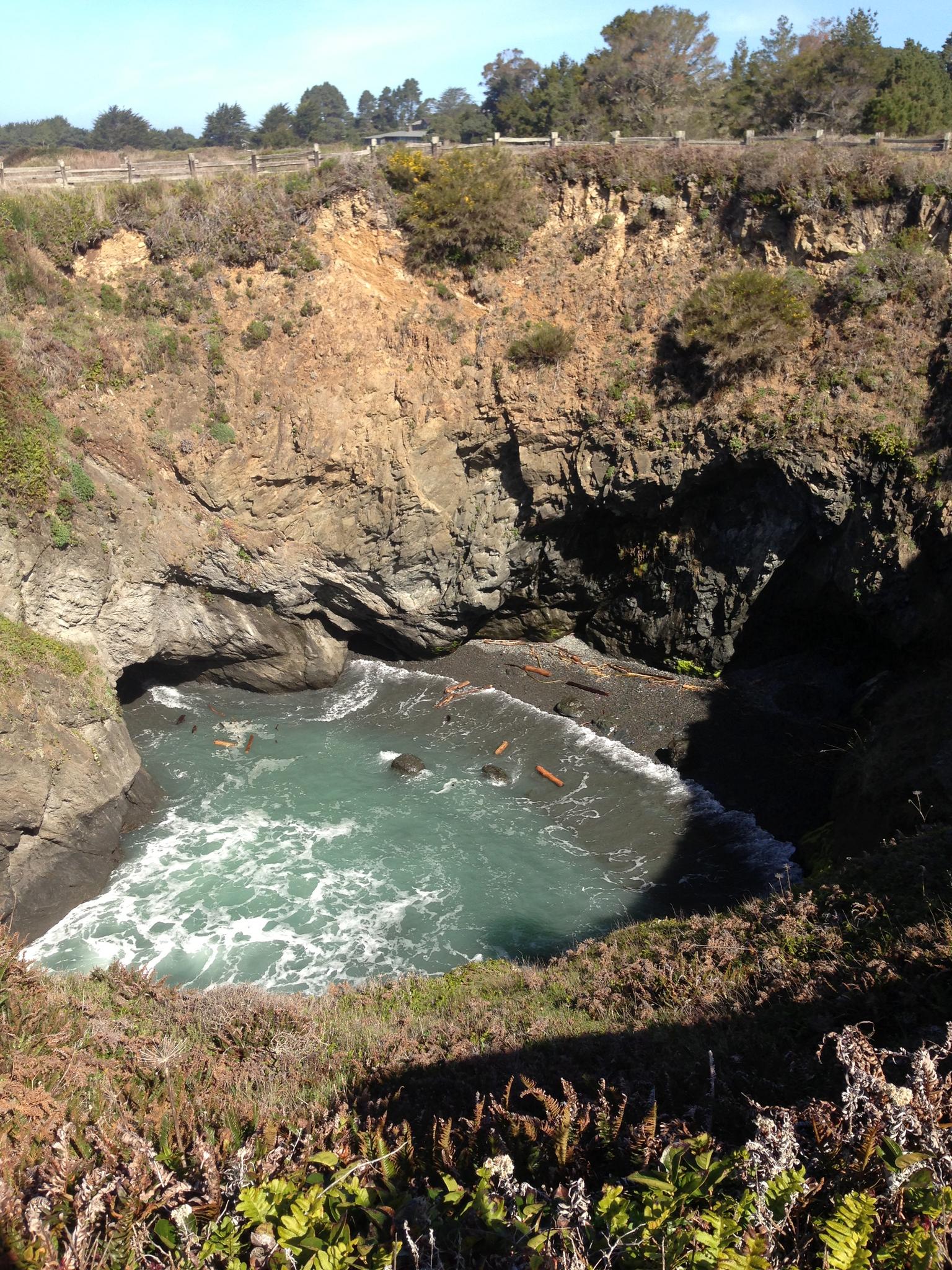 Overhead view of a deep sea cave with turquoise water and rocky cliffs.