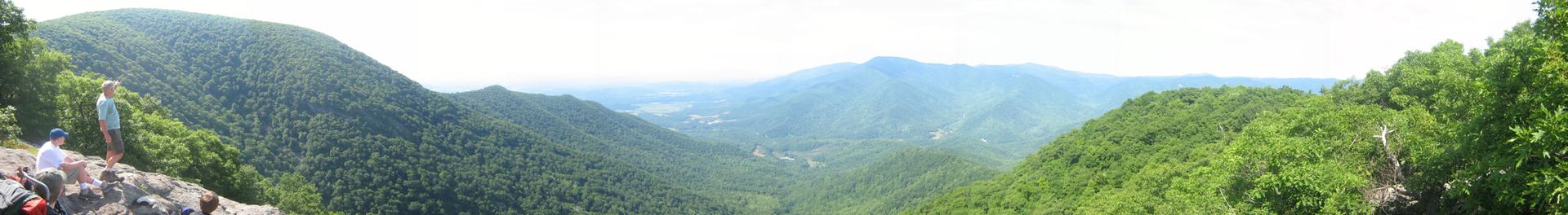 Panoramic view of a vast, lush green mountain valley with a person.
