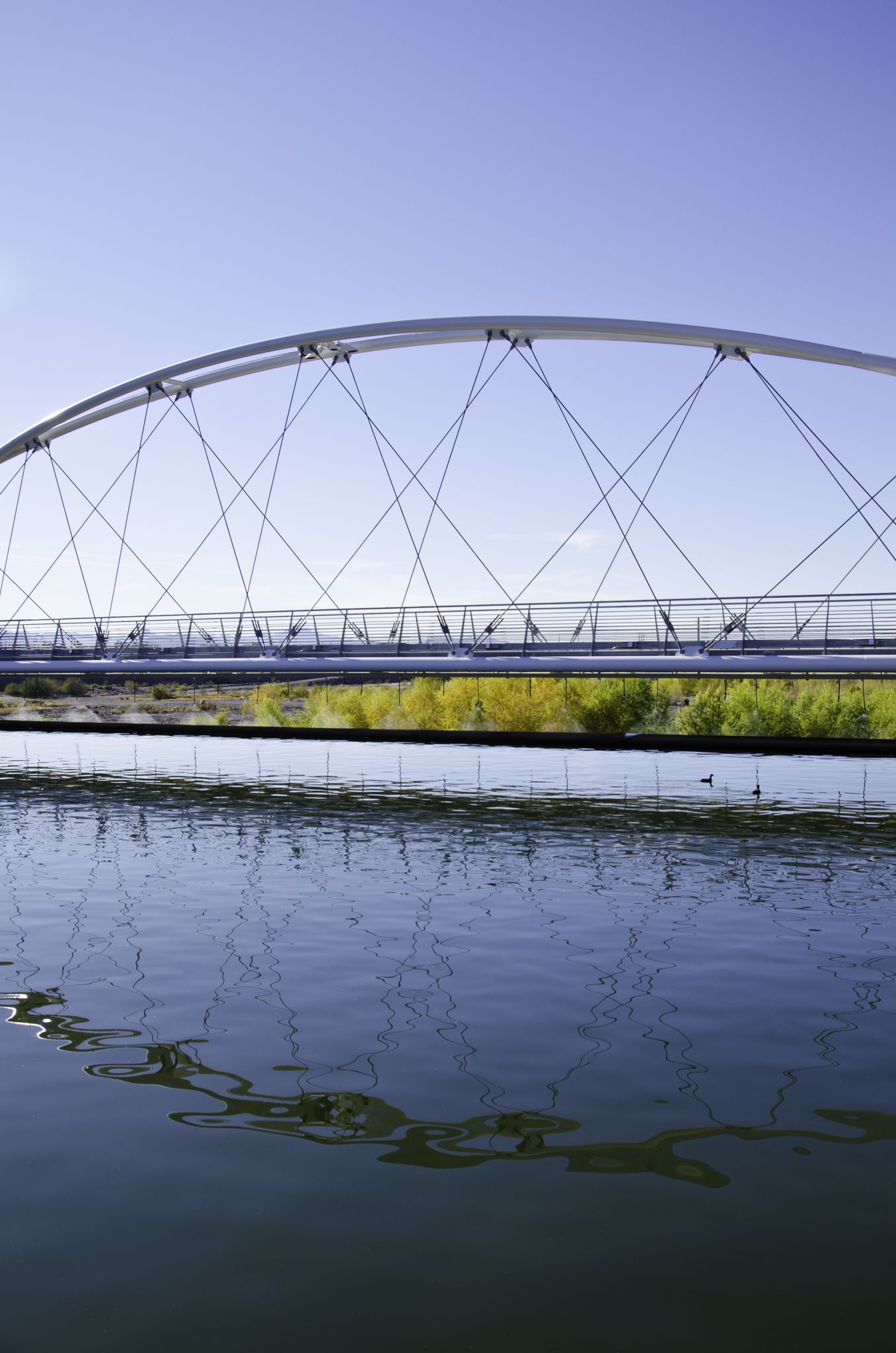 Modern arched bridge spans calm water under a clear blue sky. - Rio Salado Pathway