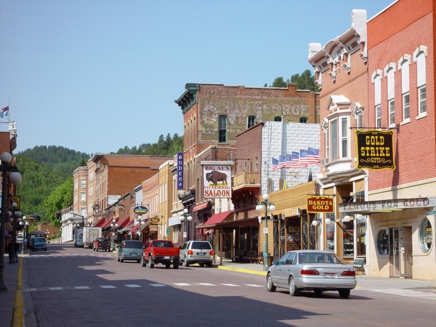 Historic main street with brick buildings, cars, and a clear blue sky.