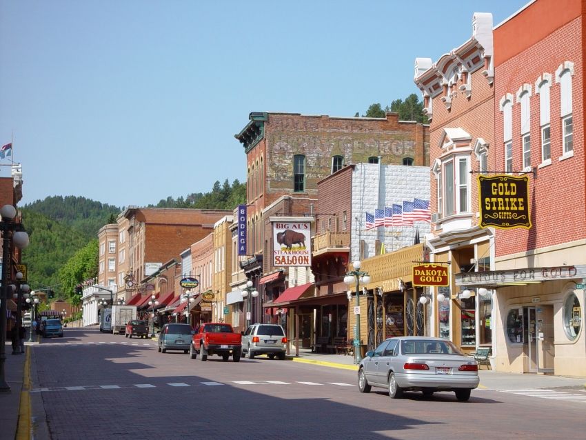 Historic main street with brick buildings, cars, and a clear blue sky. - Deadwood – Bridge loop from Deadwood