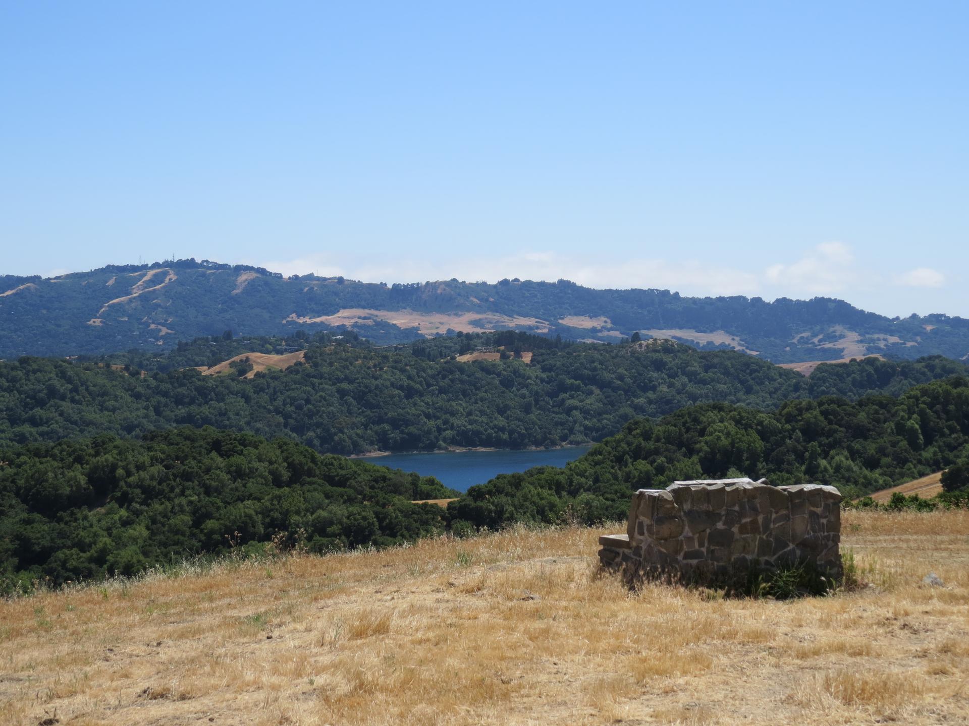 Panoramic view of a lake nestled among forested hills, with a stone structure.