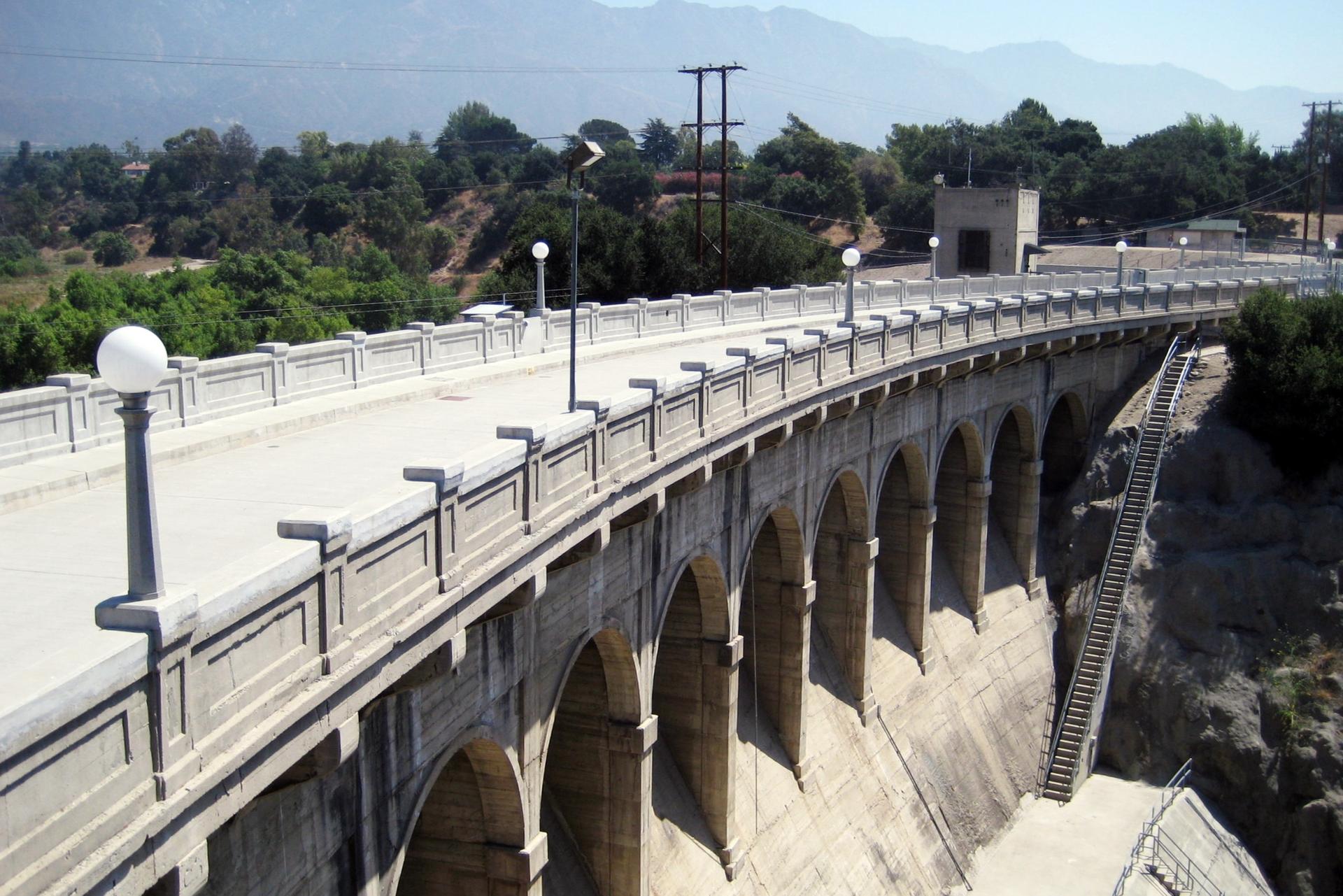 A large concrete arch bridge spans a valley under bright daylight.