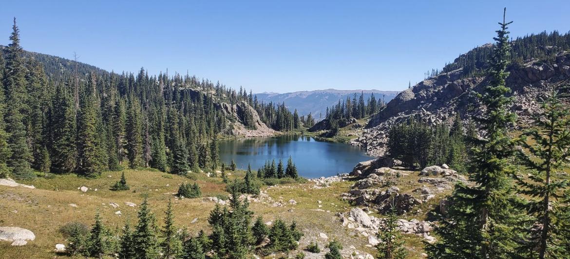 Clear blue lake nestled among pine-covered mountains under a bright sky.