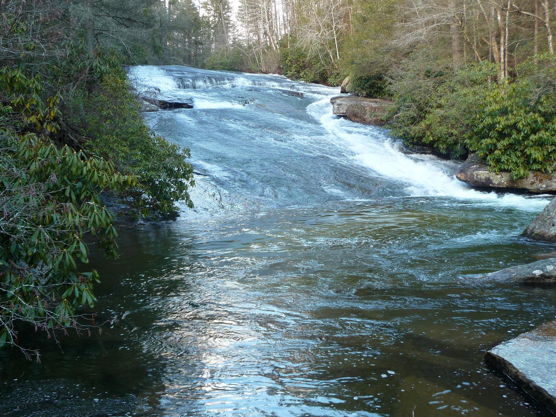 Wide, multi-tiered waterfall cascades over rocks into a flowing river.