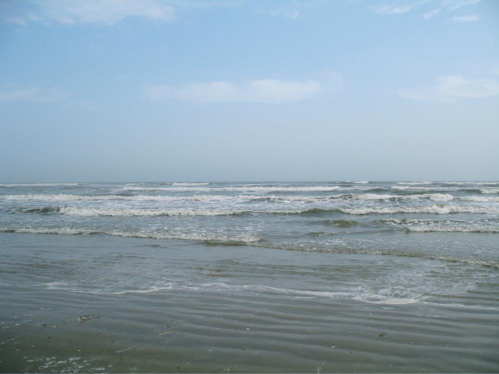 Ocean waves rolling onto a sandy beach under a light blue sky.