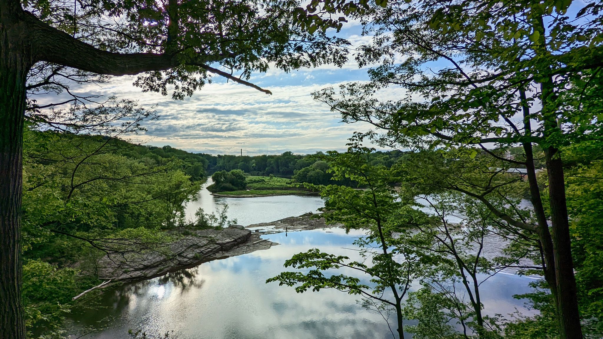 Lush green trees frame a calm river with reflections under a bright sky. - Winooski River to Shelburne Pond loop