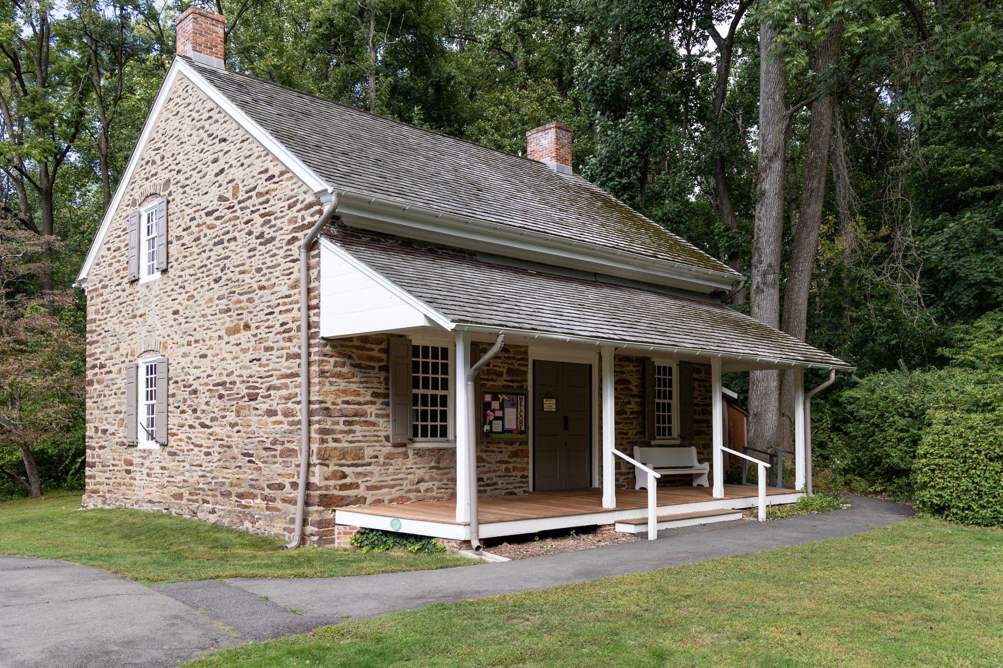 An old stone house with a white porch surrounded by green trees. - Stony Brook loop from Princeton University