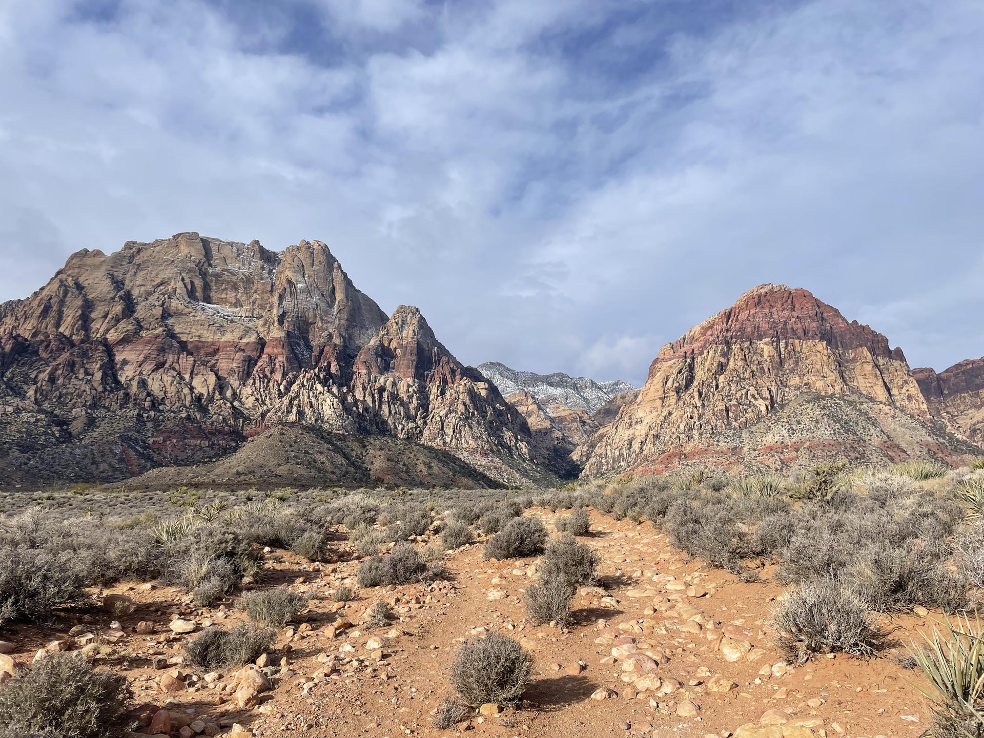Vast desert landscape with towering red and tan mountains under a cloudy sky.