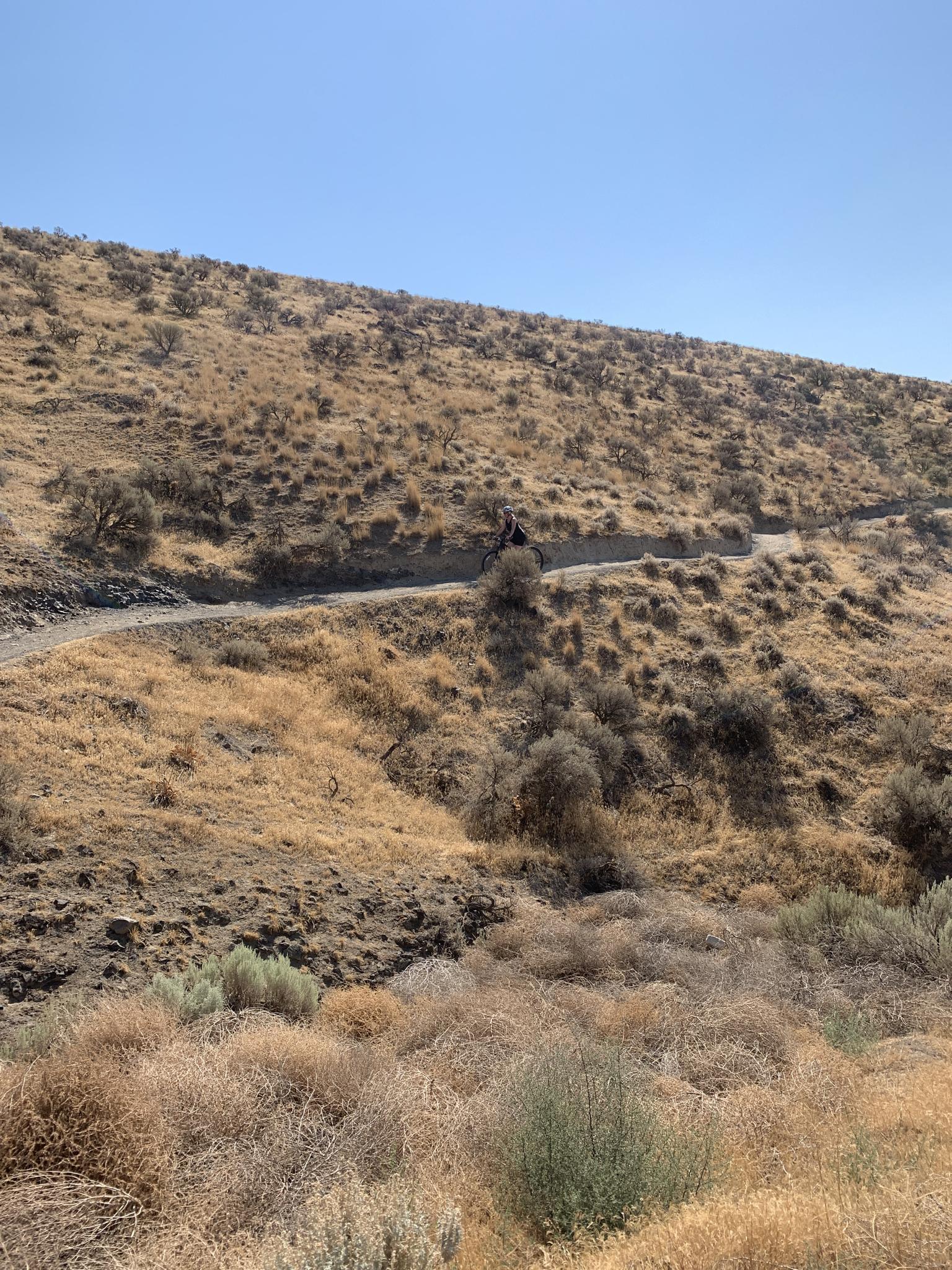 Distant person on a dirt path winding through dry, hilly terrain.