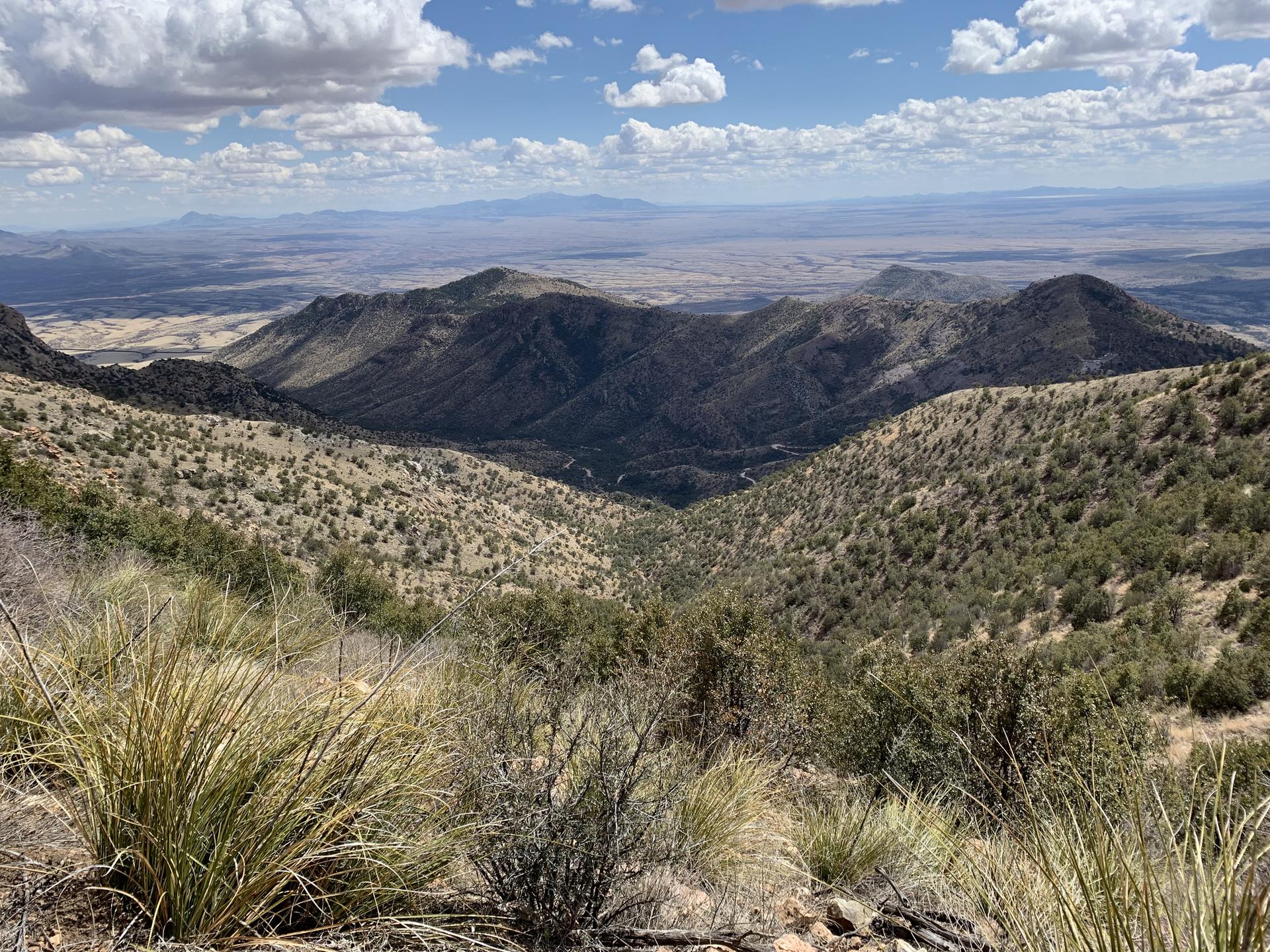 Wide mountain valley with dry vegetation under a partly cloudy sky.