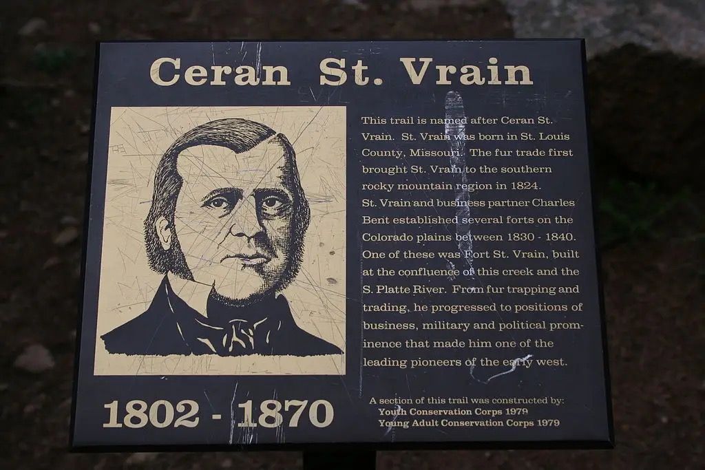 A close-up of a dark informational sign with text and a man's portrait. - Ceran St. Vrain and Miller Rock Loop
