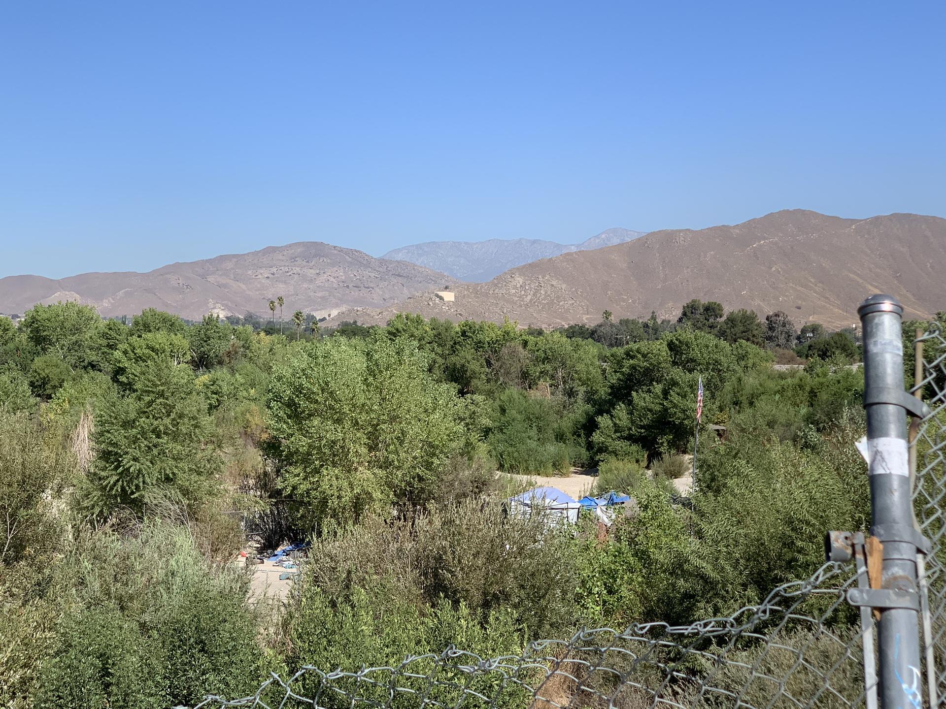 Lush green valley, arid mountains, clear blue sky, seen through a chain-link fence.