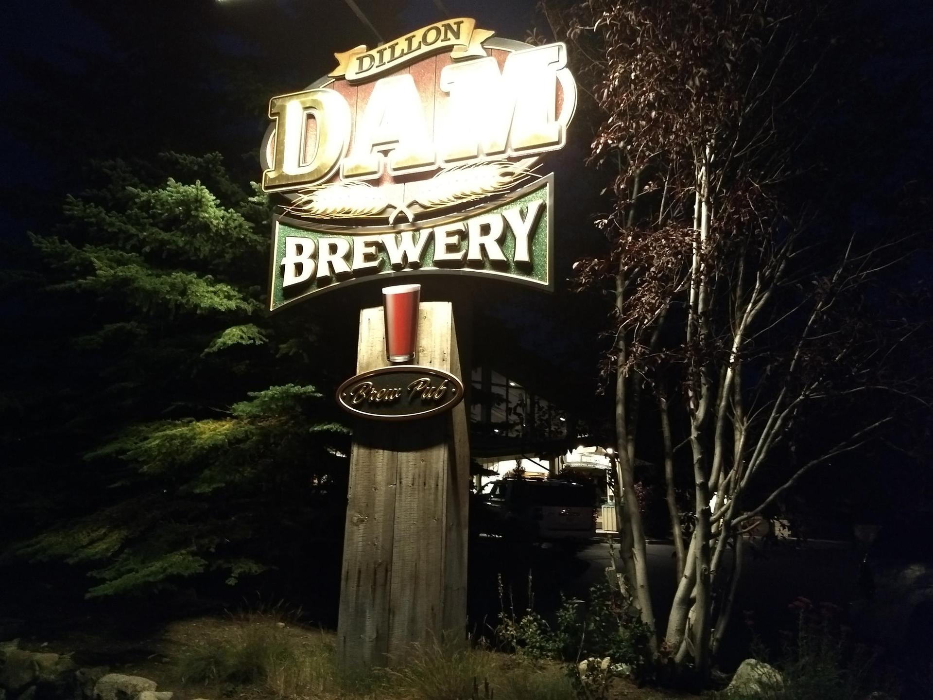 Brightly lit brewery sign at night, surrounded by dark trees.