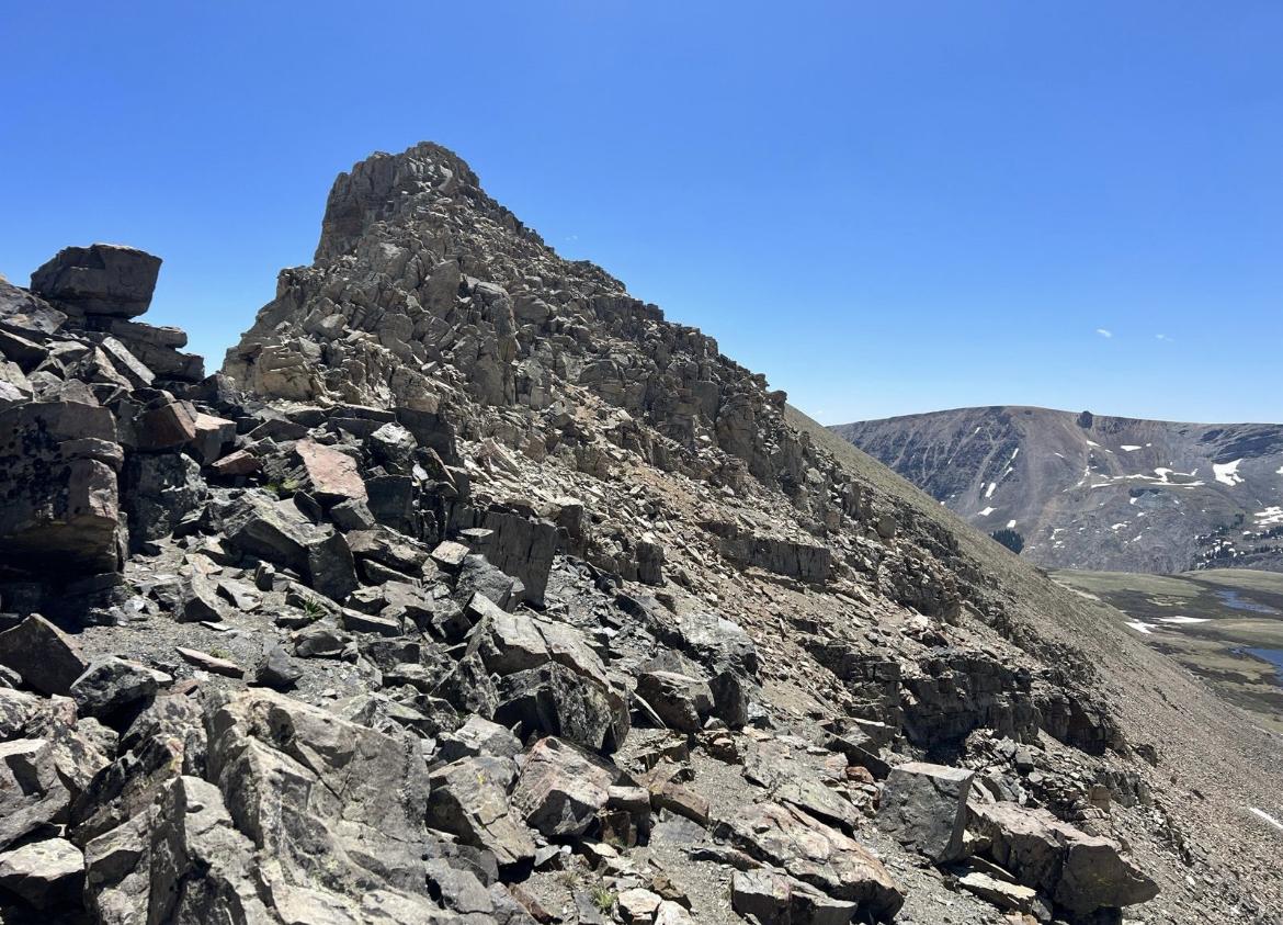 Steep, rocky mountain peak and scree slope under bright, clear blue sky.