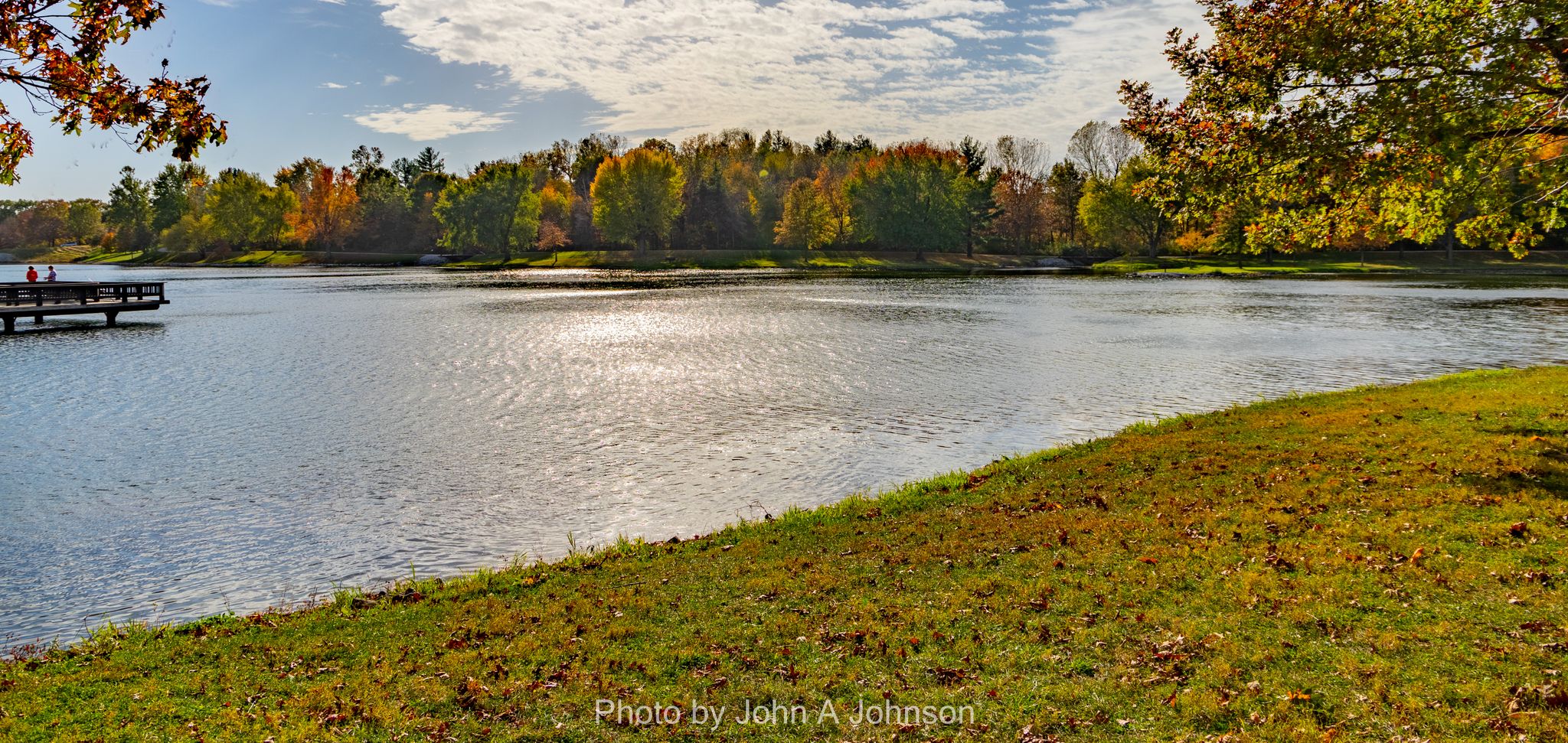 Sunny lake with a dock, autumn trees, and two distant figures. - Lake and Valley View Trail Loop