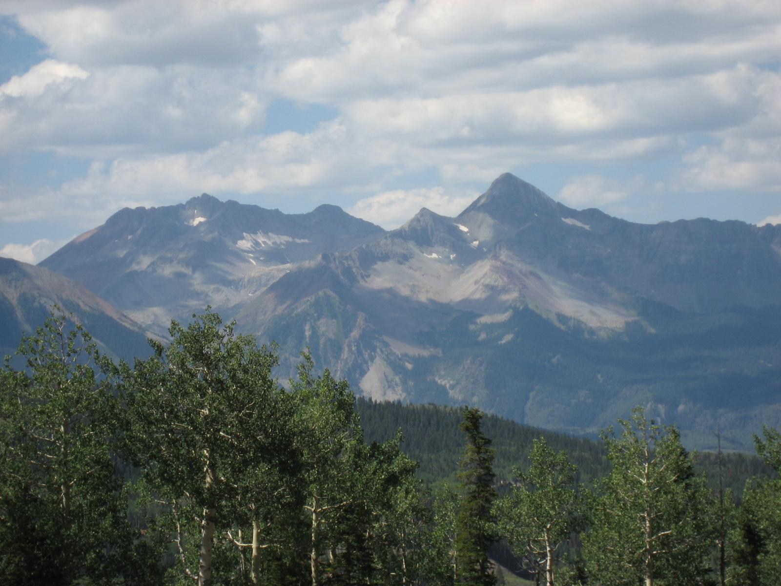 Rugged mountain peaks with snow patches above a green forest.