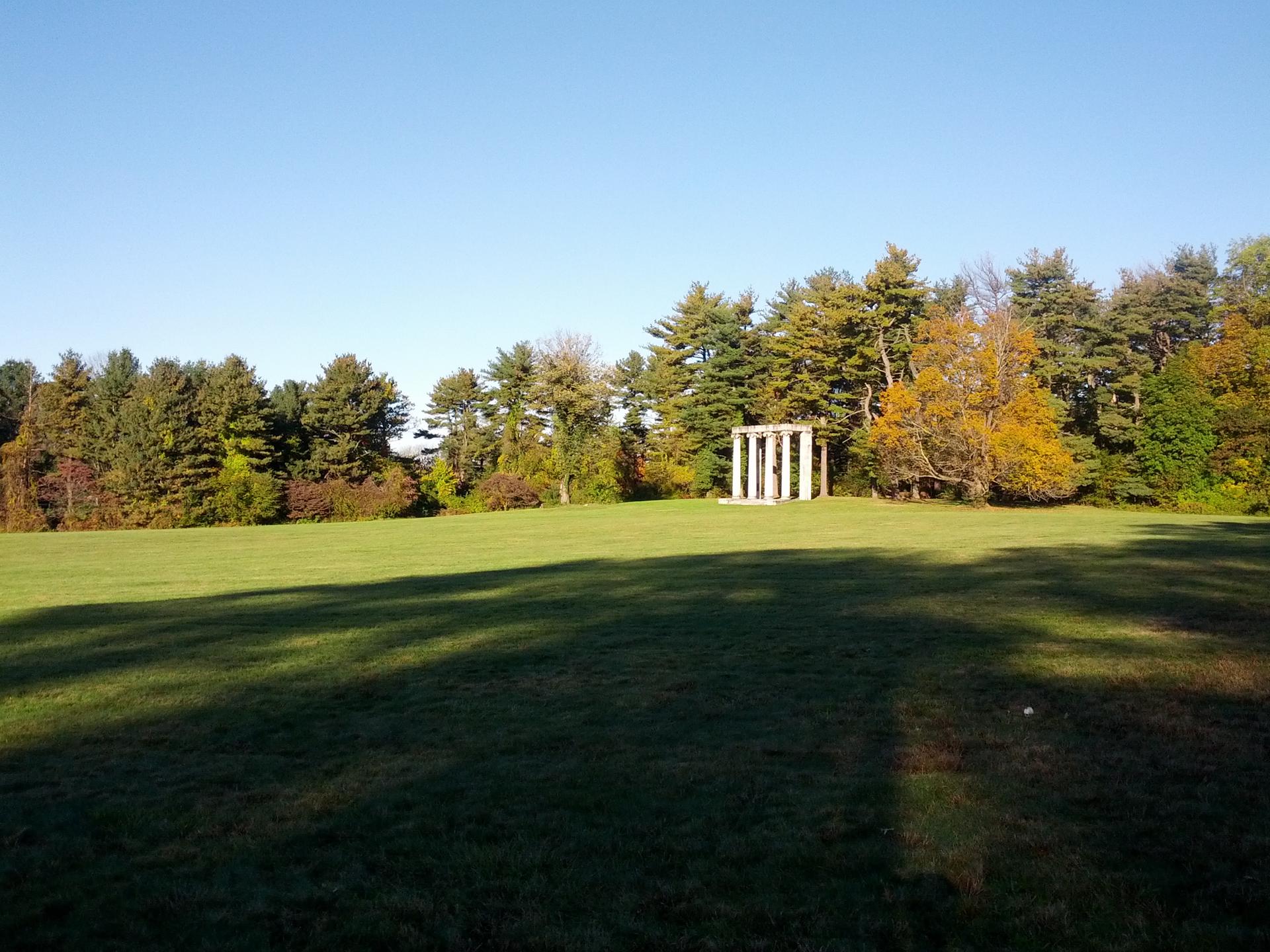 White structure in a sunlit green field bordered by trees.