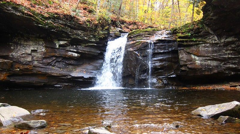A beautiful waterfall cascades into a clear pool surrounded by rocky cliffs. - Seneca Creek Trail