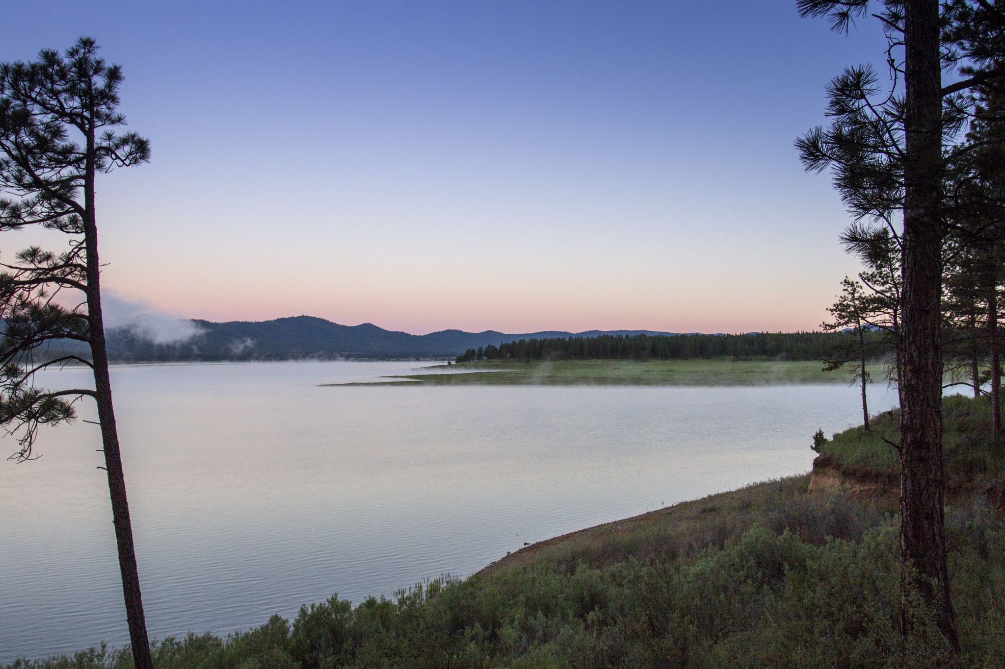 Misty lake at dawn with trees in foreground and mountains in background. - Phillips Lake Loop Trail