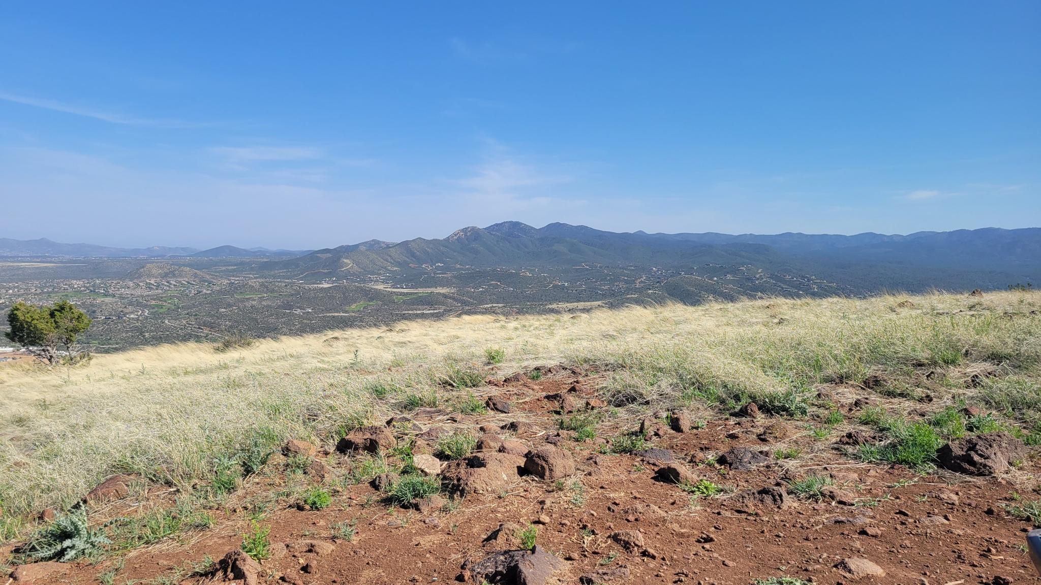 Rocky foreground with dry grass, leading to distant green mountains under clear sky.