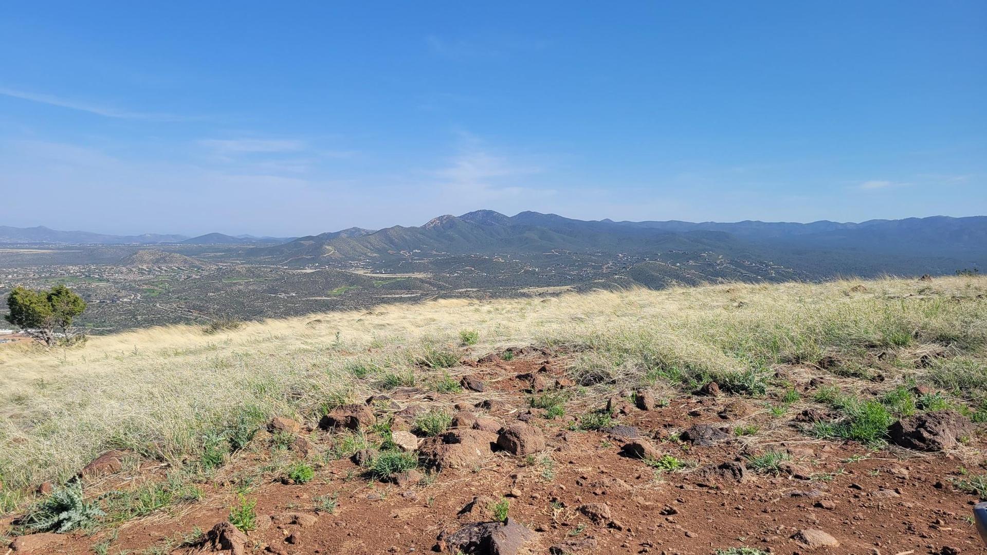 Rocky foreground with dry grass, leading to distant green mountains under clear sky.