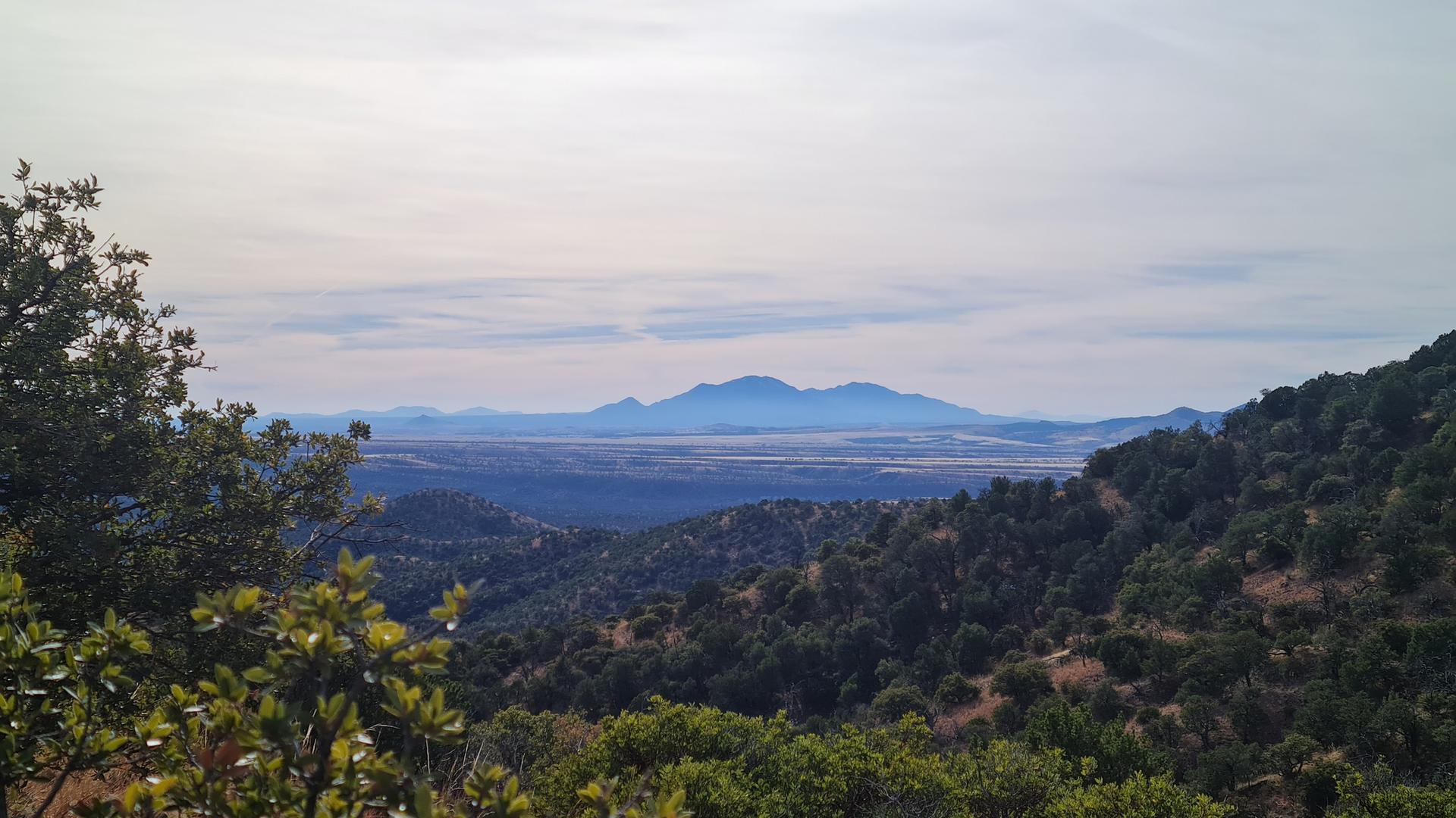 Panoramic view of forested hills and distant mountains under a cloudy sky.
