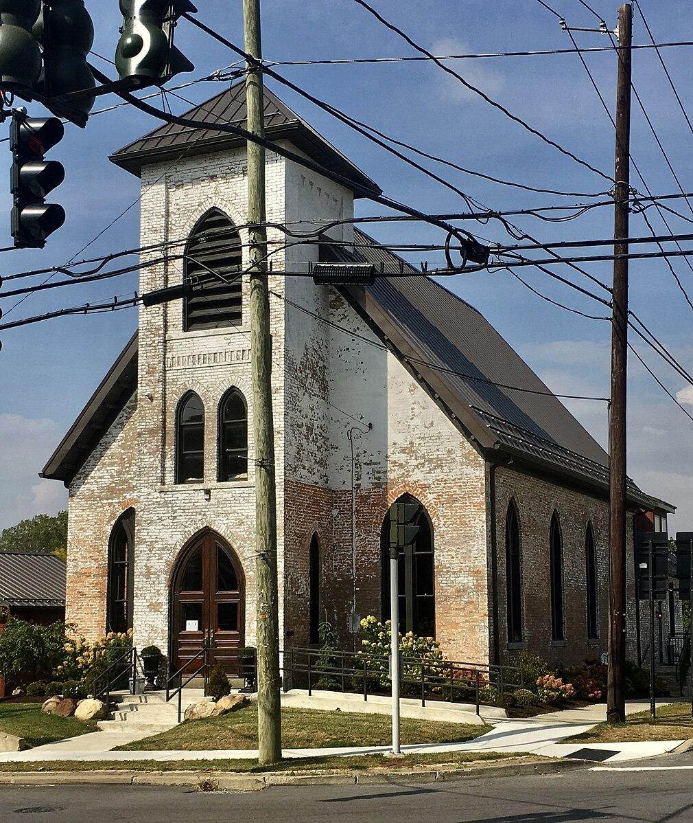 An old brick church with a white facade and tall steeple on a sunny day.