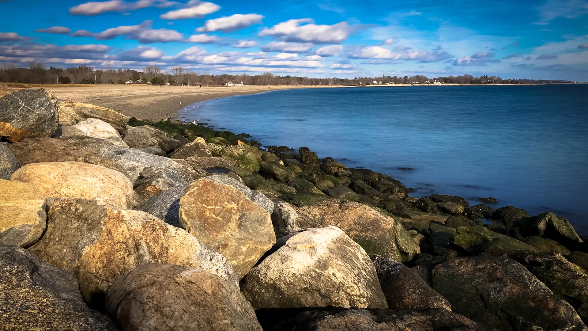 Sunny day with blue sky over a rocky coastline and sandy beach.