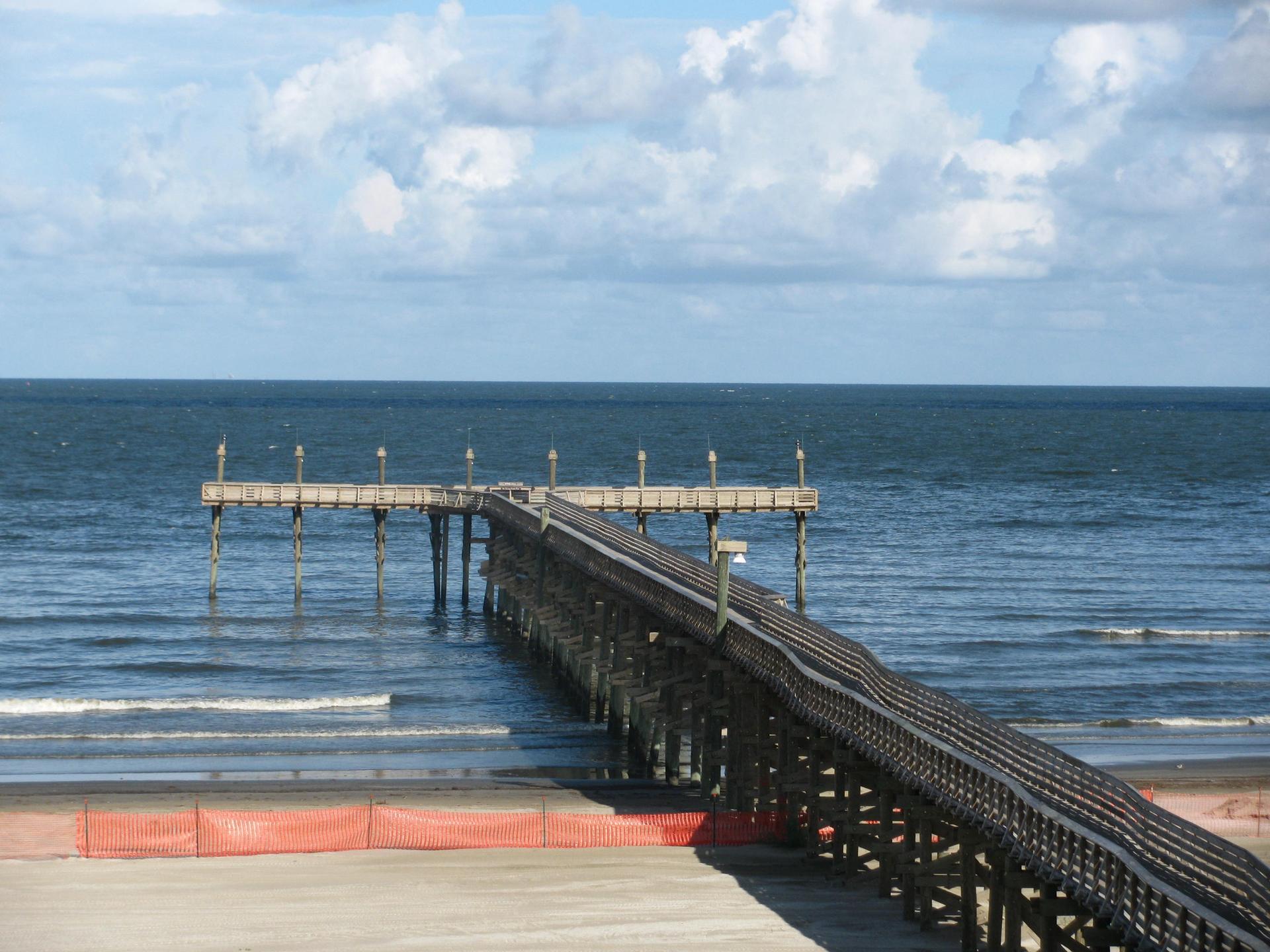 Wooden pier stretching into the ocean from a beach under a cloudy sky.