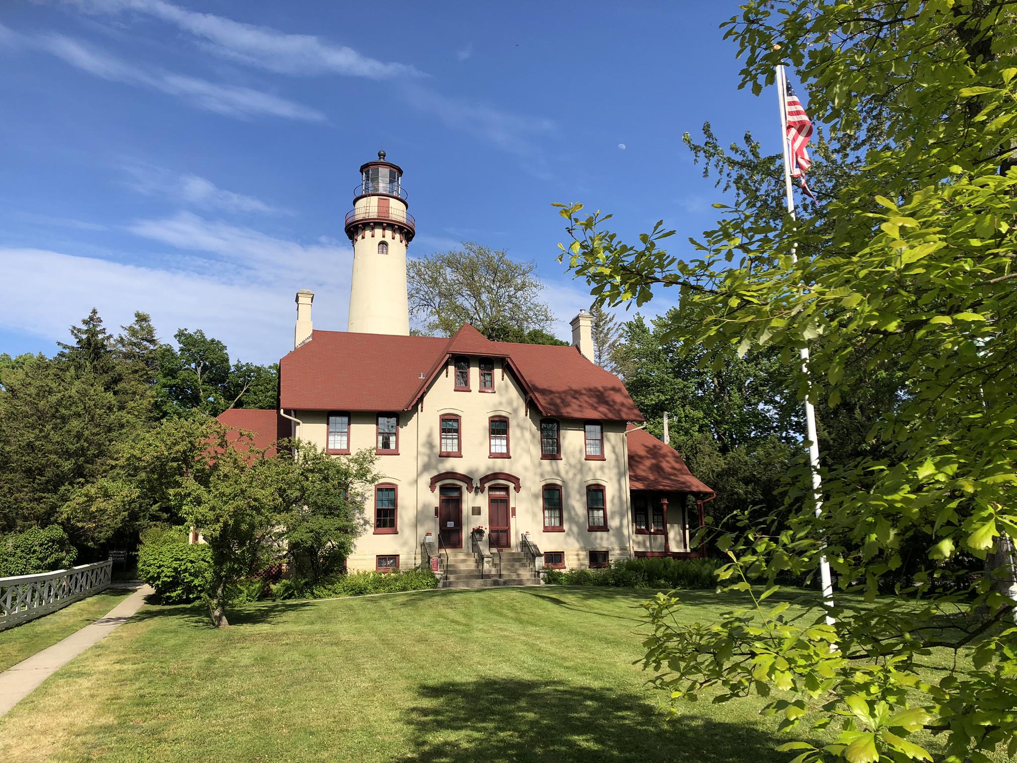 A tall lighthouse next to a large house on a sunny green lawn.