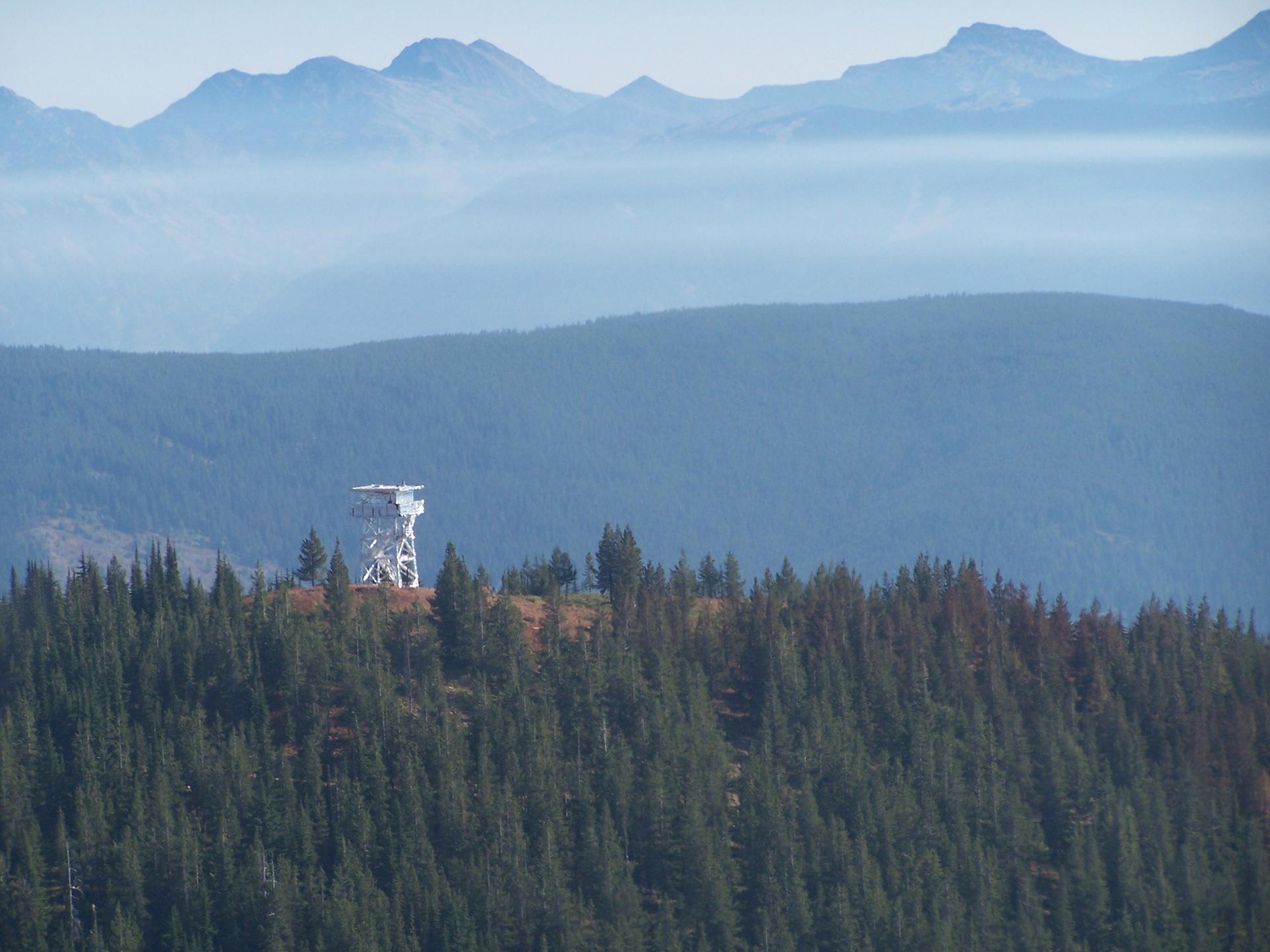 White tower on a forested ridge with hazy mountains in the background.
