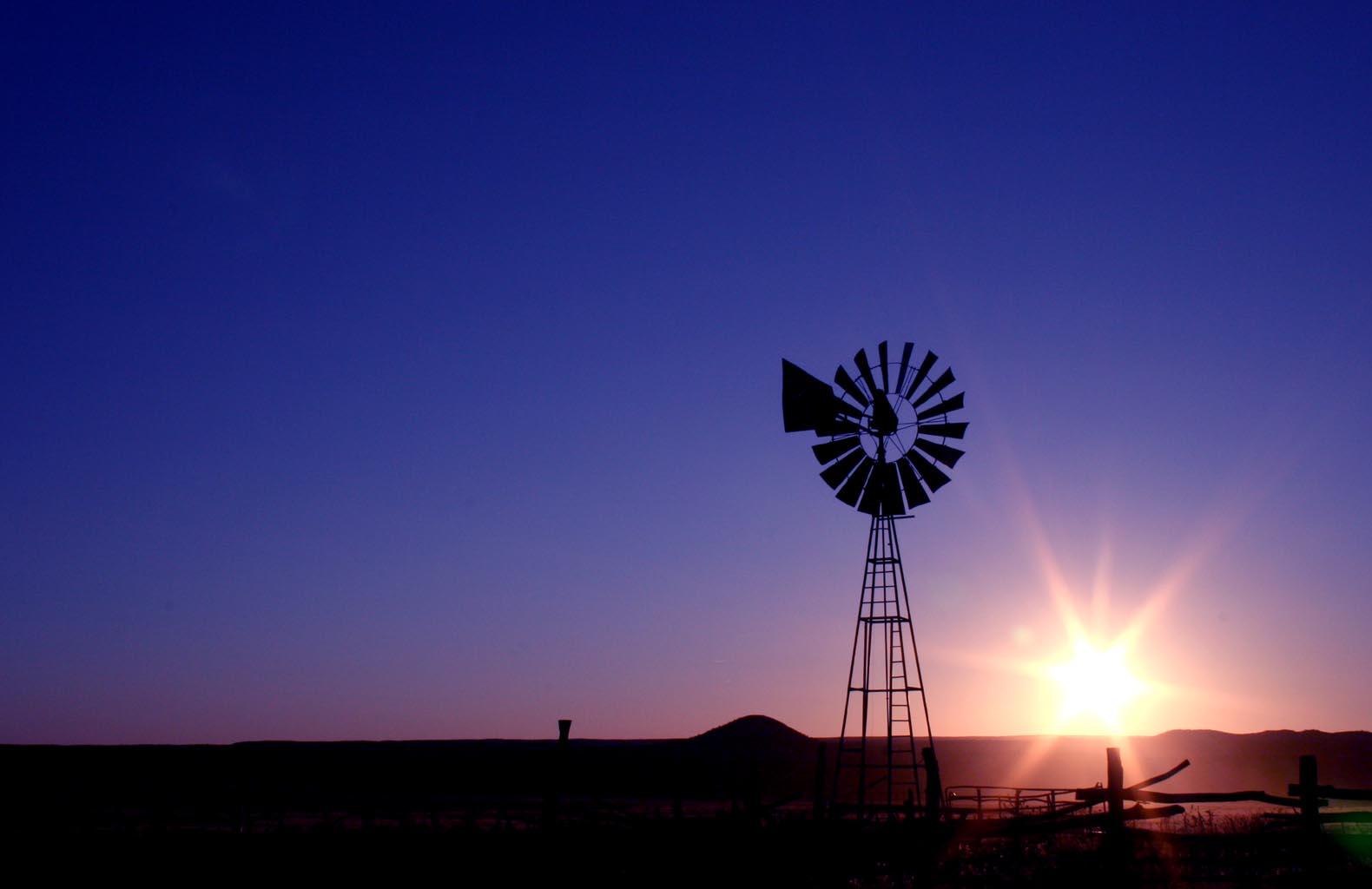 Windmill silhouette against a vibrant purple and orange sunset sky over a flat landscape.