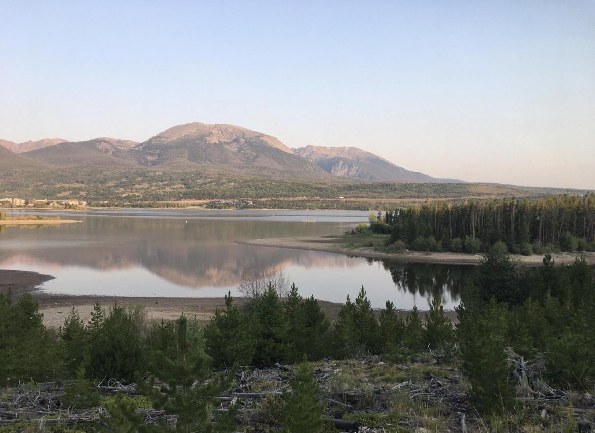 Calm lake reflecting distant mountains under a clear, soft sky.