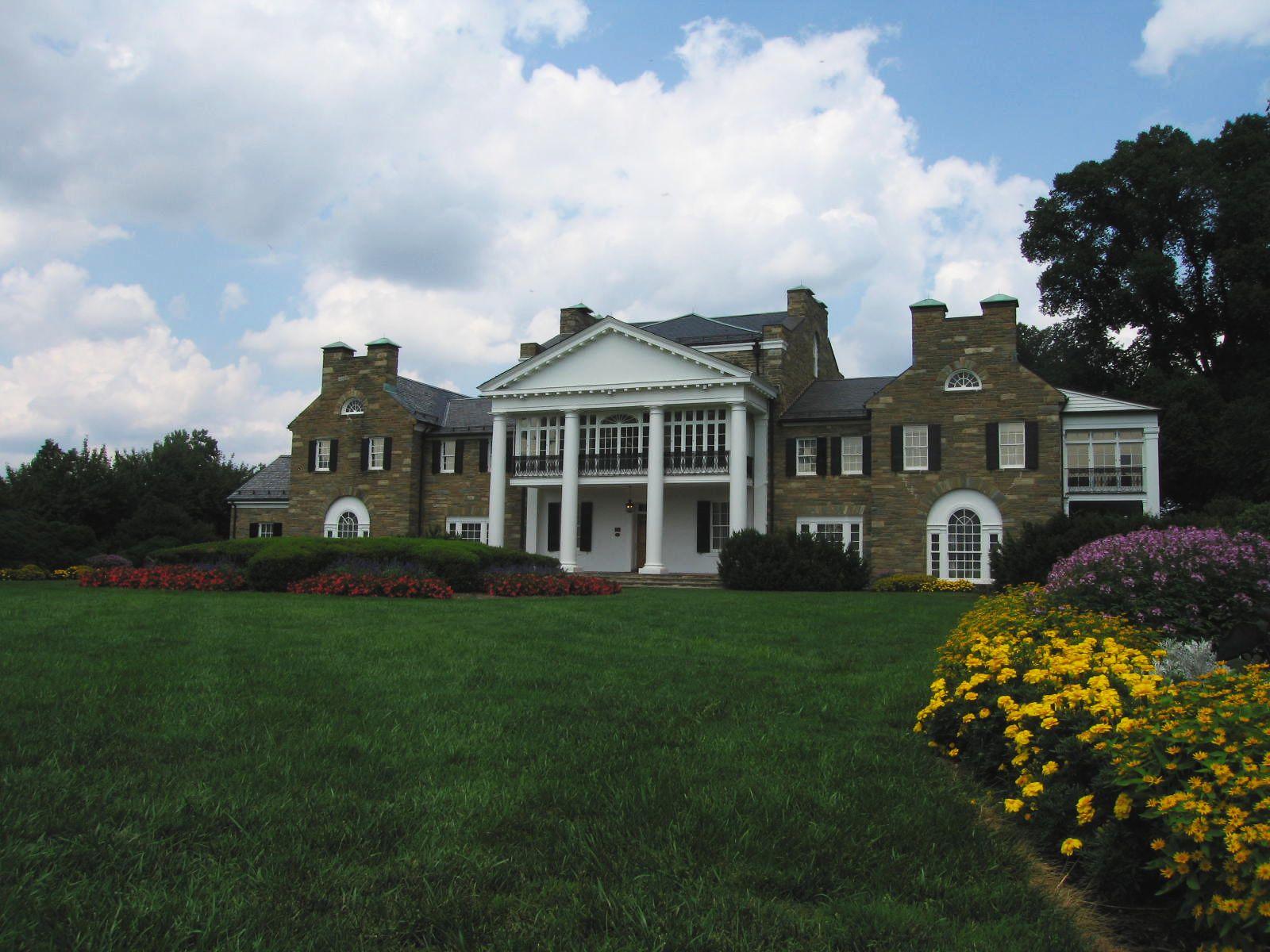 A large stone mansion with white columns, green lawn, and colorful flowers.