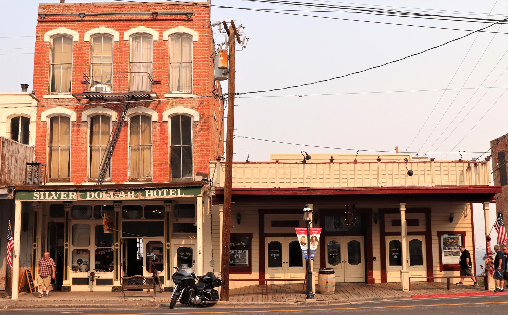 Historic brick and wooden buildings line a street with a motorcycle and people.