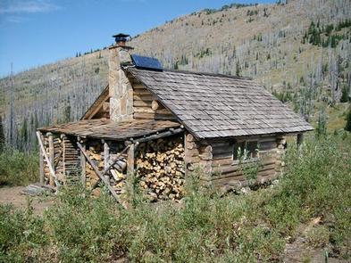 Rustic log cabin with stacked firewood and solar panel under bright daylight.