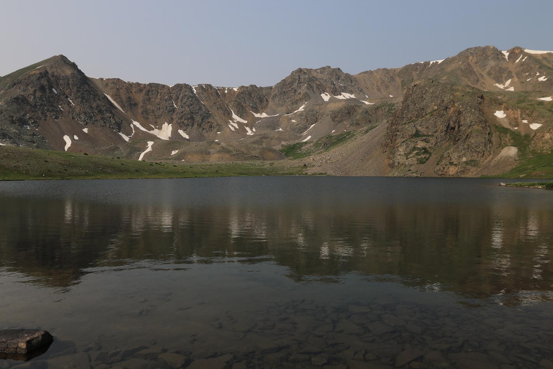 Wide mountain lake with clear water and distant rocky peaks under soft light.