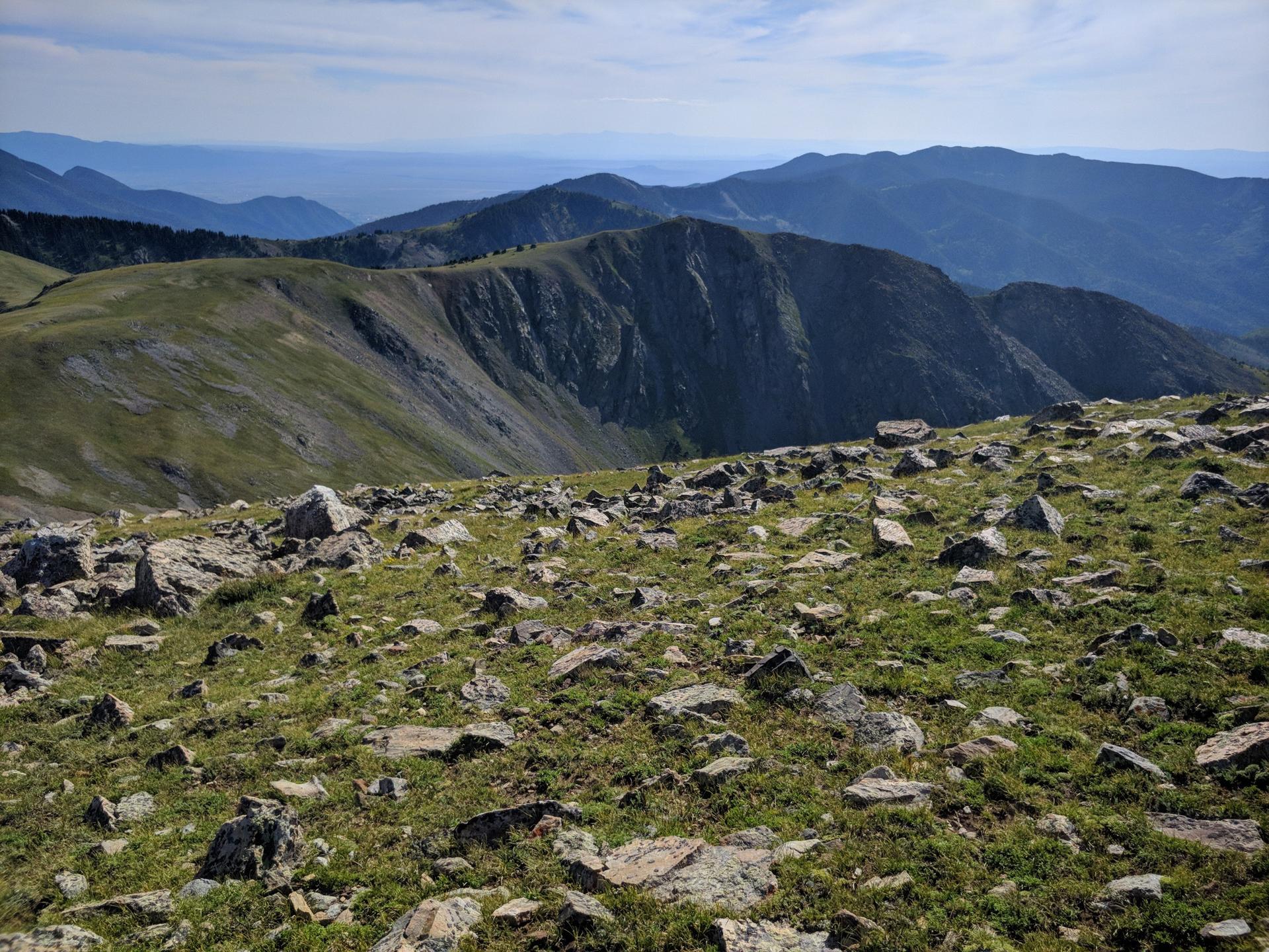 A rocky, grassy mountain landscape with a small hut and distant hazy mountains.