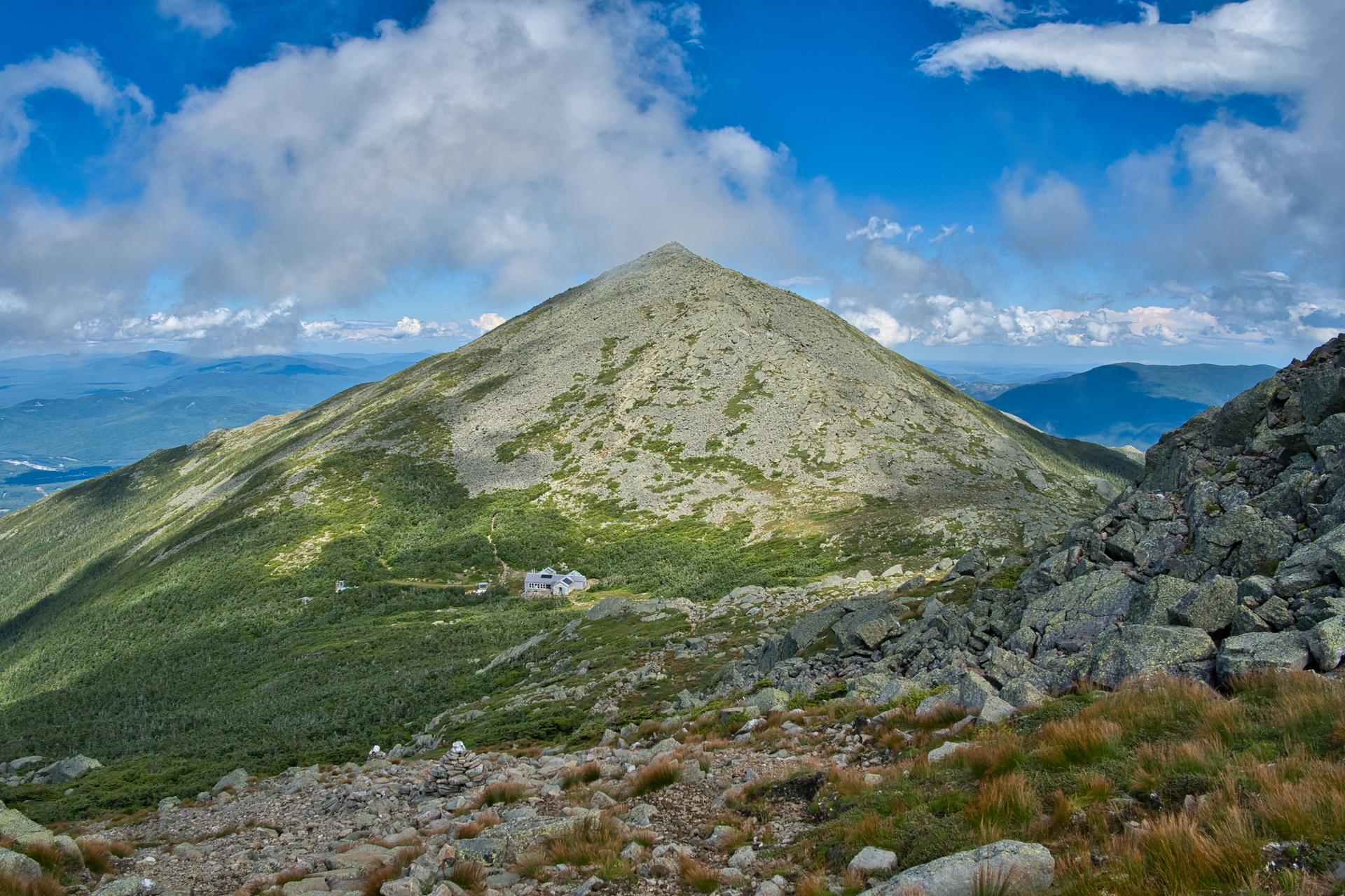 Steep, rocky mountain peak with a small building below, on a bright day.